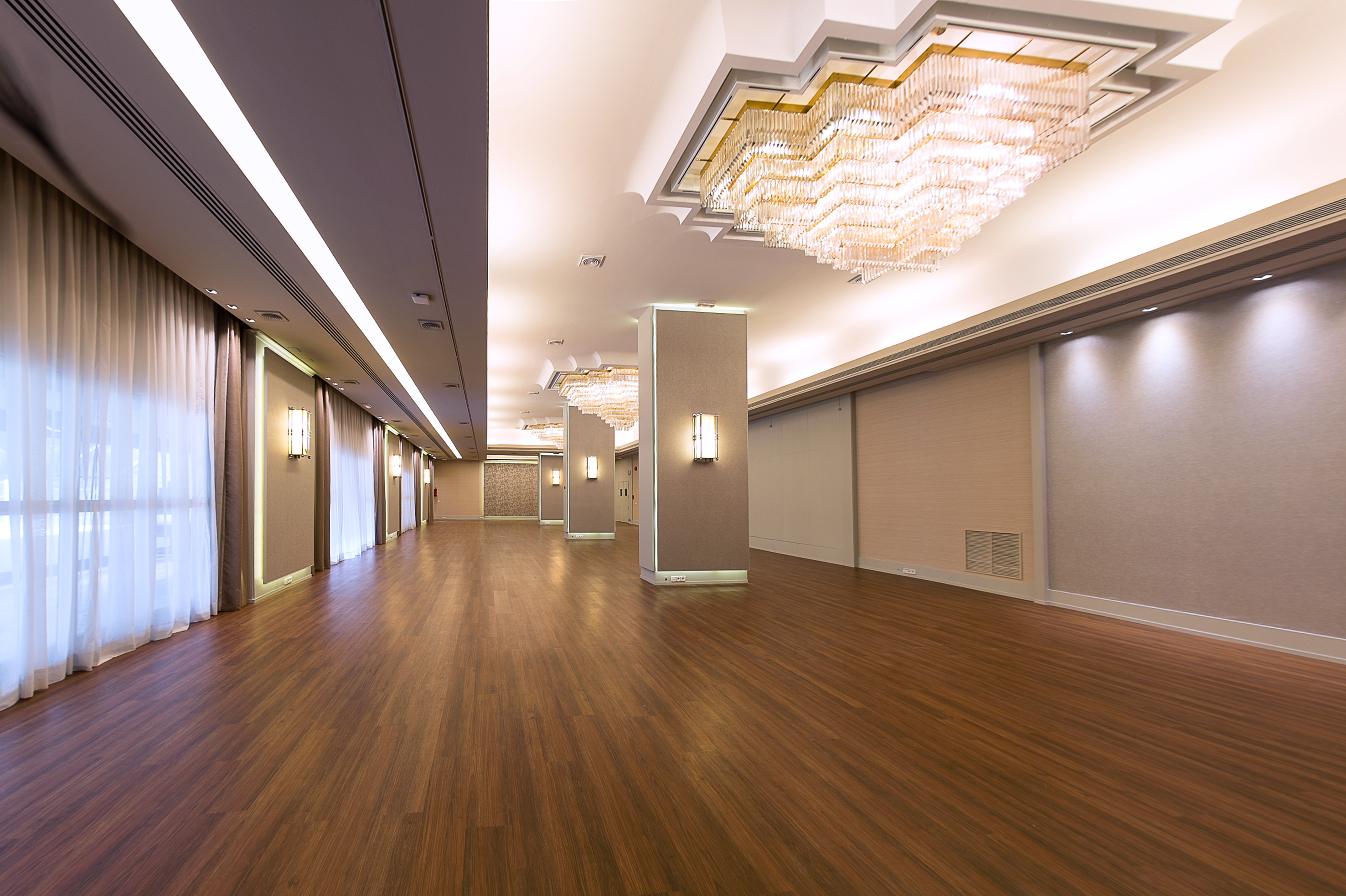 Empty modern event hall with wooden floor, large chandeliers, and elegant lighting.