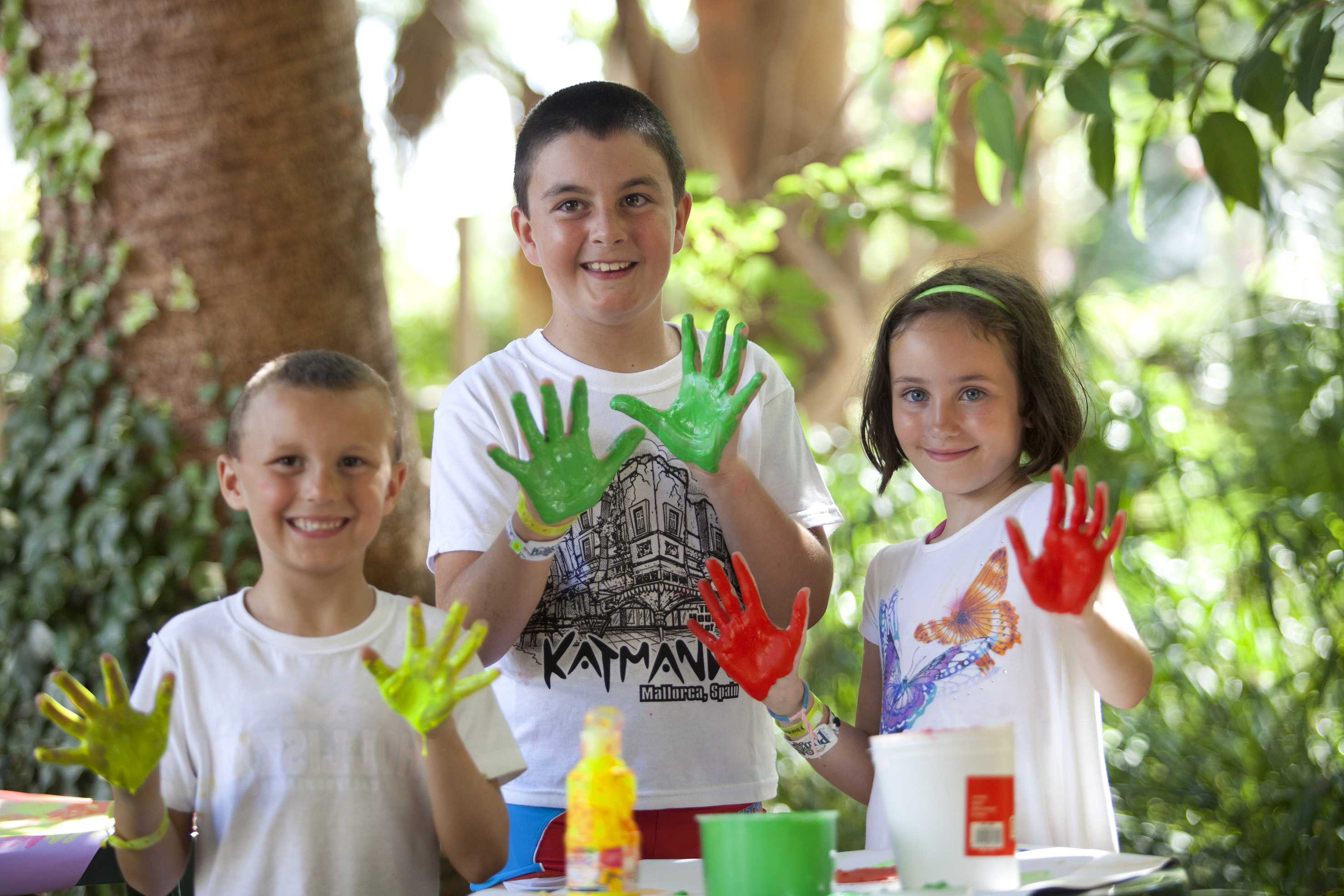 Smiling kids with colorful painted hands enjoying an outdoor art activity.
