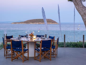 a table set up with blue chairs and a tree overlooking the water
