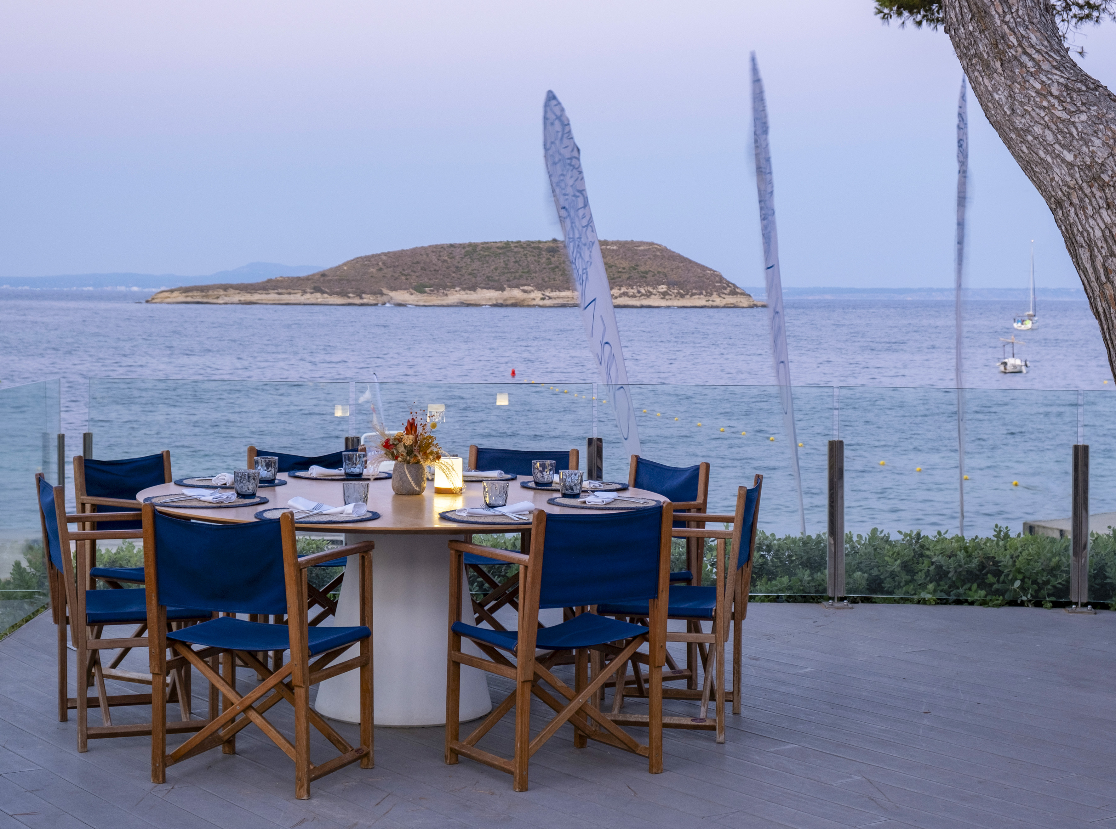 Oceanfront dining table, blue chairs, sea view, and distant island at dusk.
