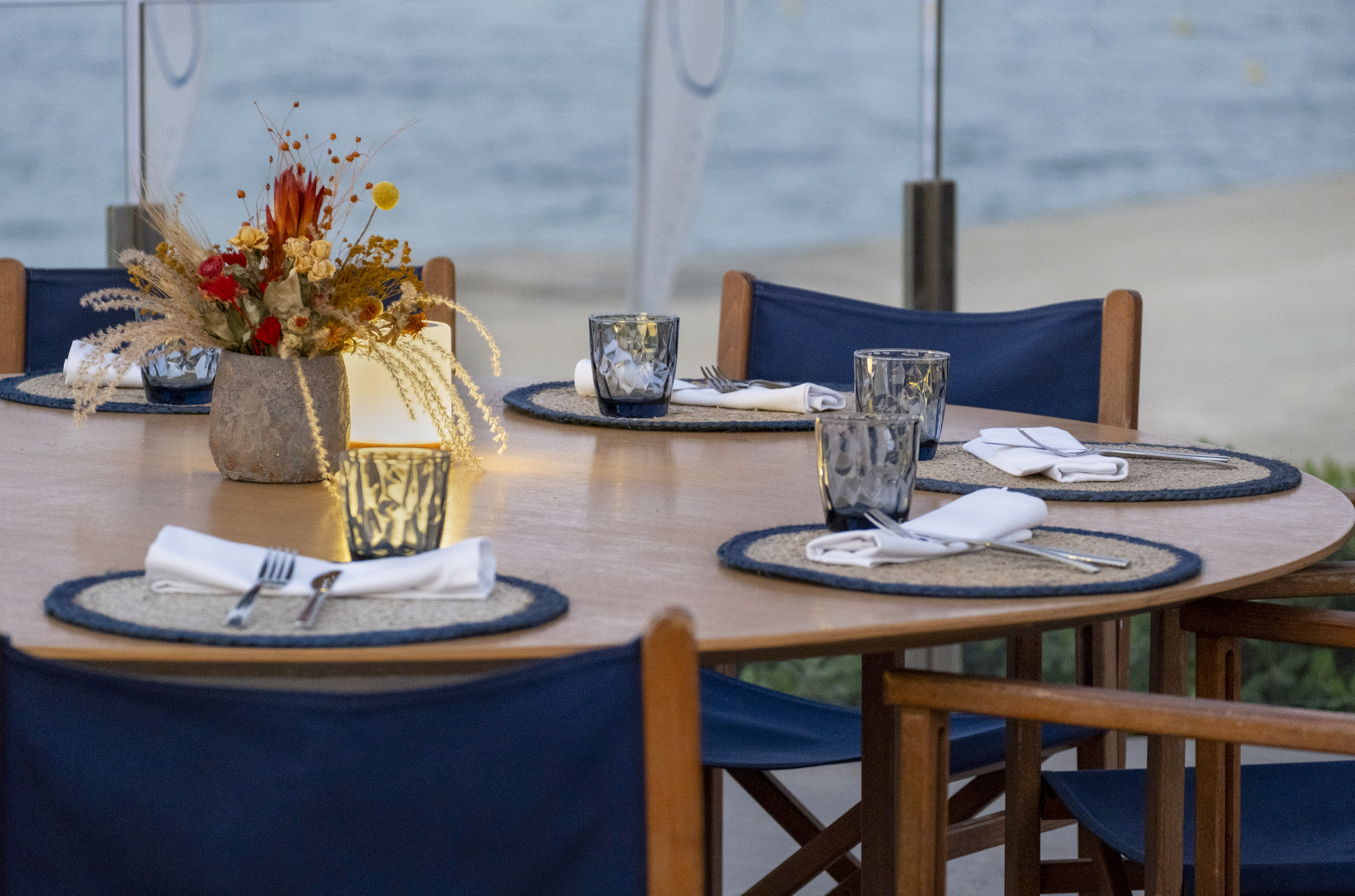 Outdoor dining table setting with dried flowers and blue chairs.
