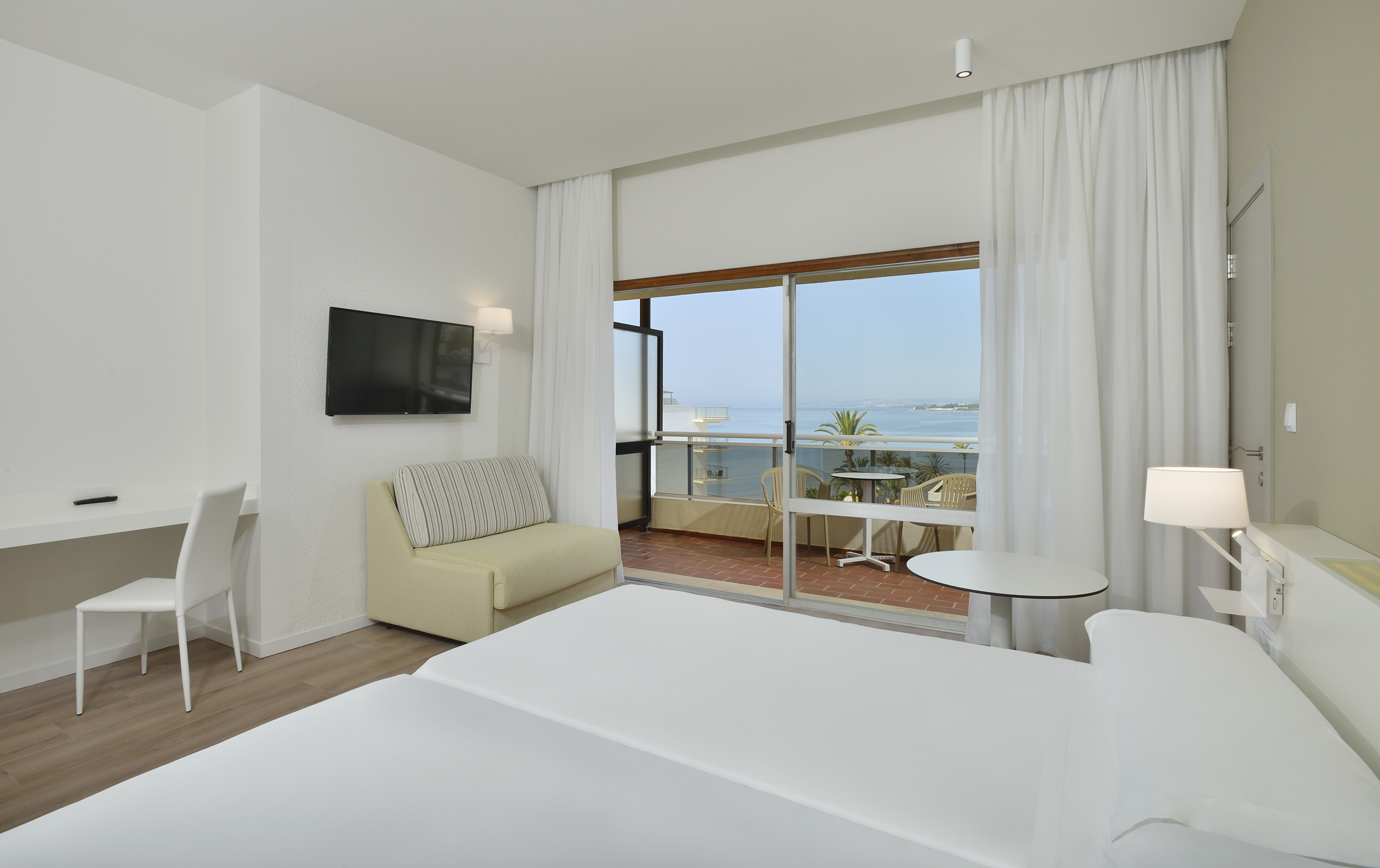 Bright hotel bedroom with twin beds, balcony, desk, and ocean view.