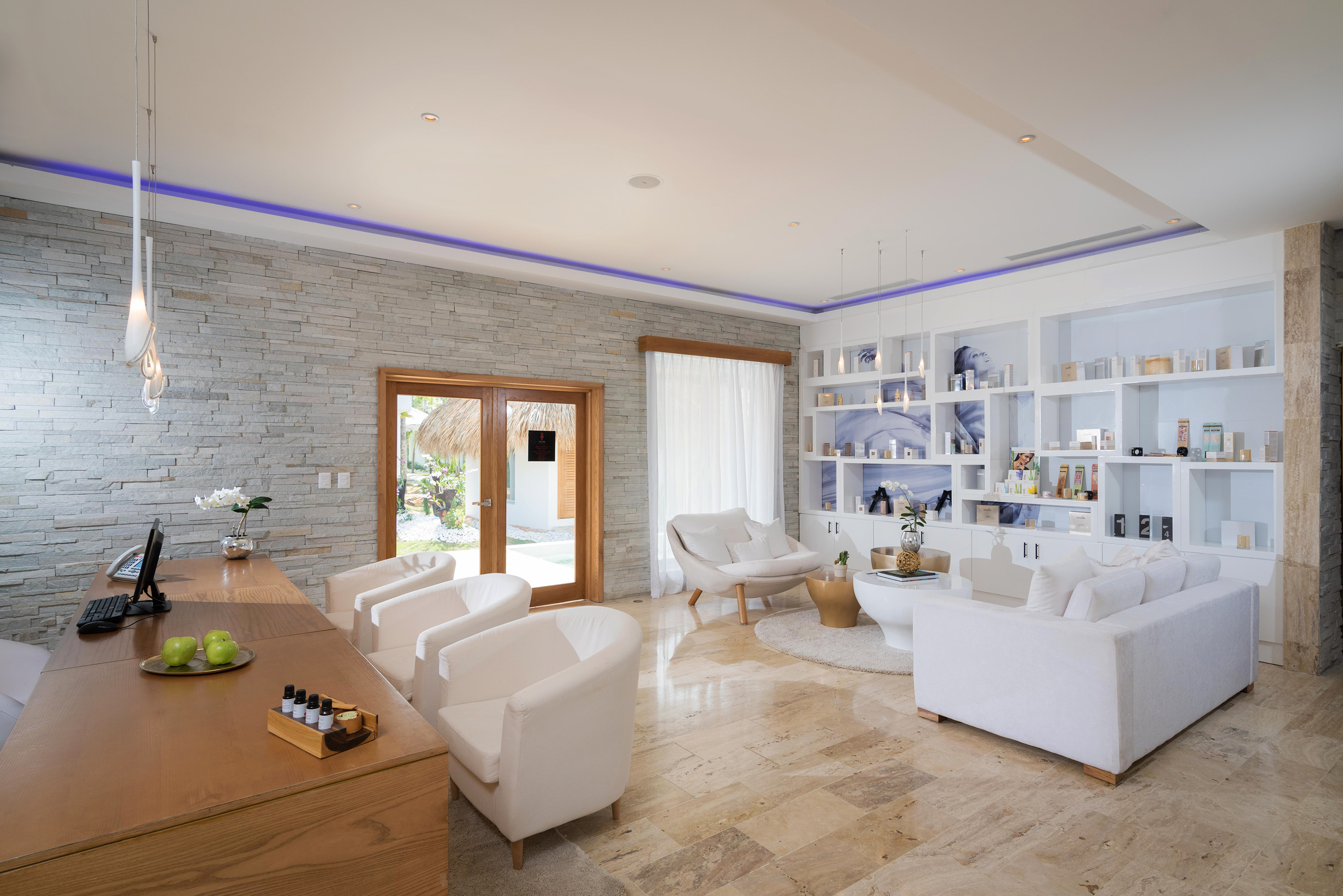 Elegant spa reception lounge with white seating, wood desk, product display.