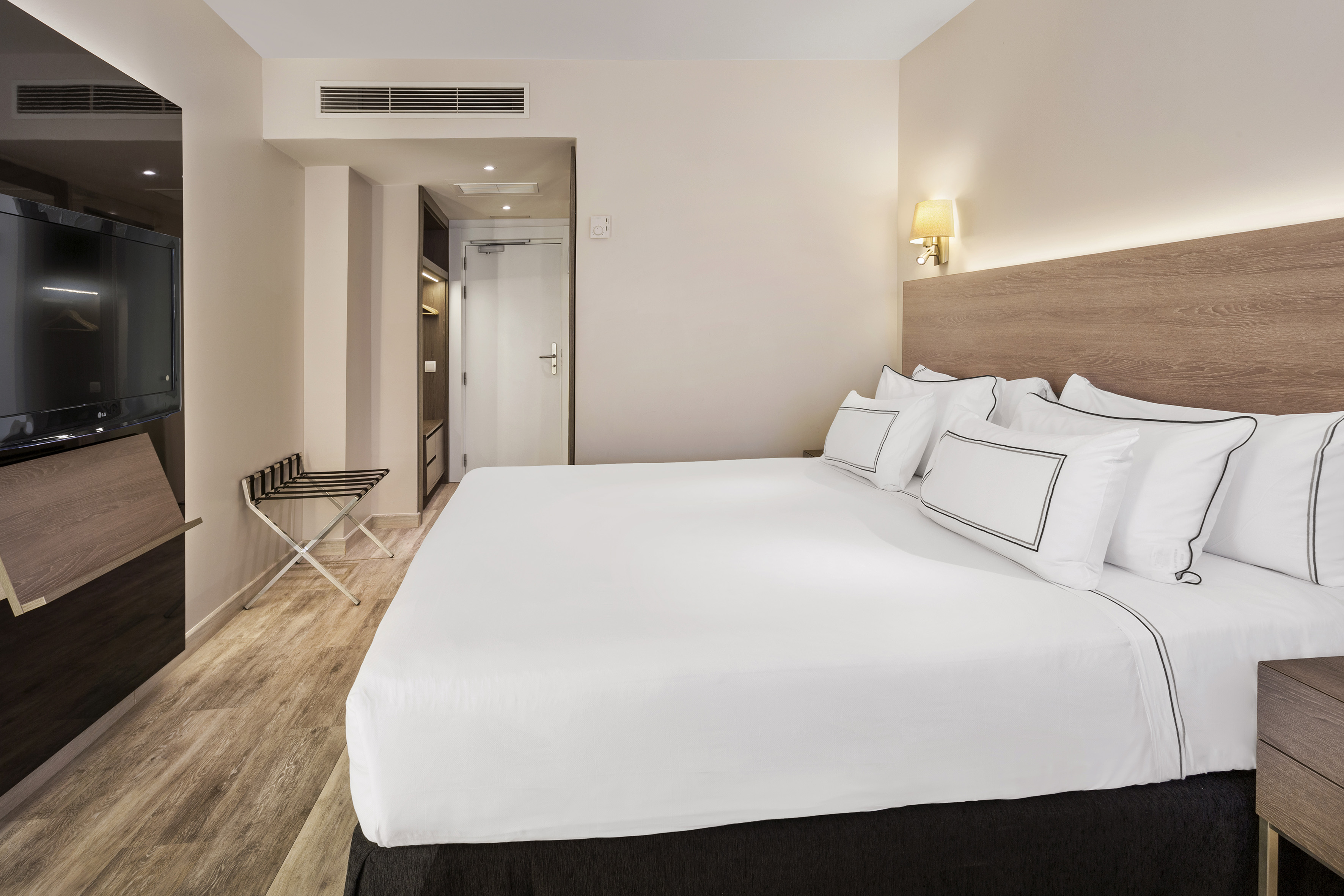 Modern hotel room with king bed, white bedding, TV, and luggage rack.