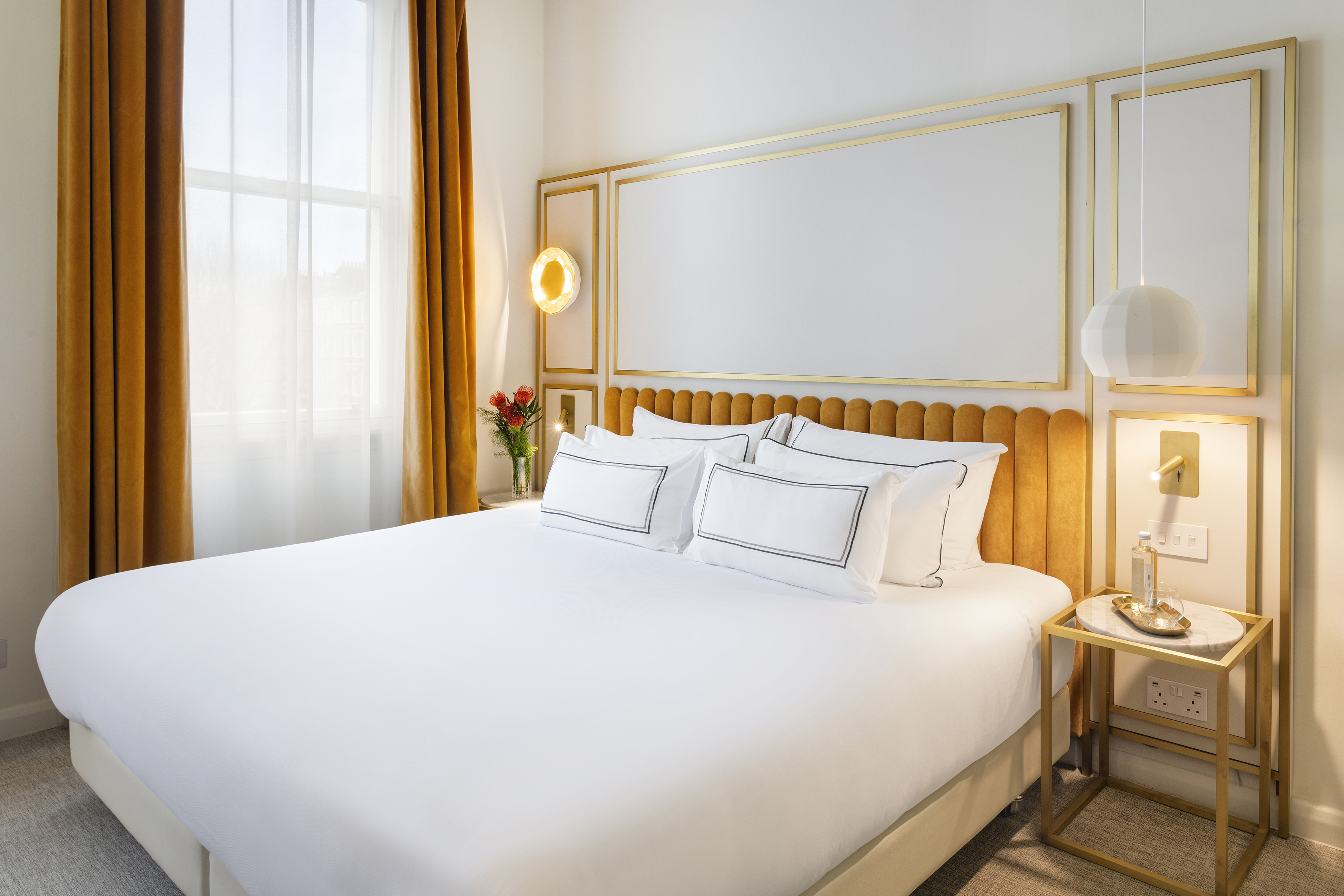 Modern hotel bedroom with gold velvet headboard, white bed, and curtains.