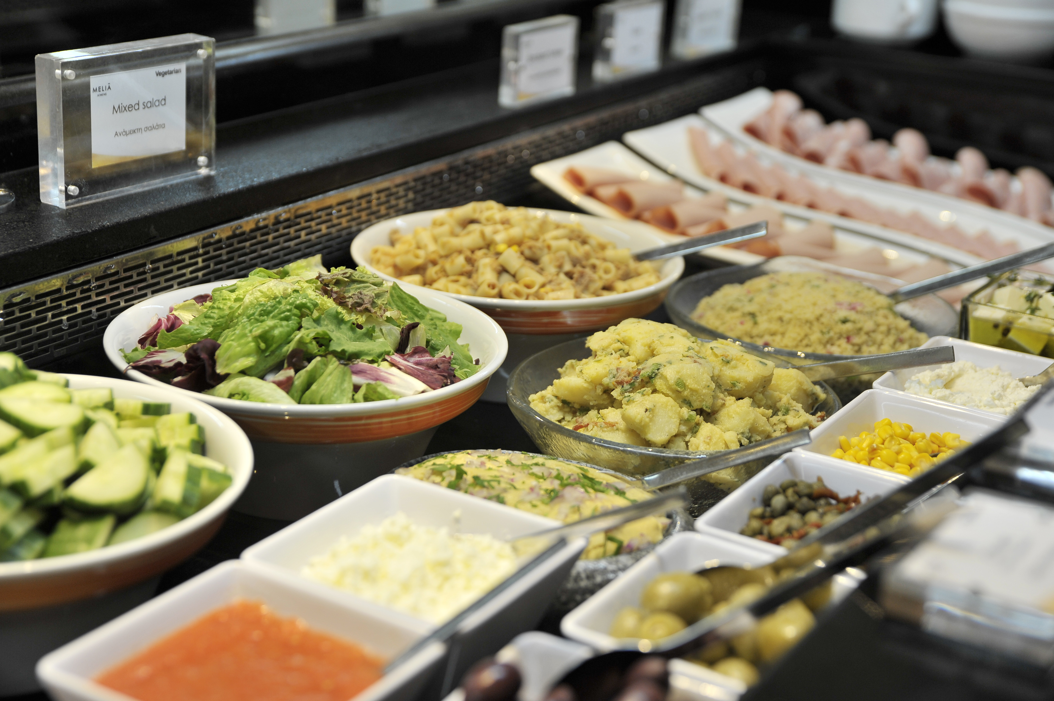 Hotel buffet: fresh salads, potato salad, pasta, deli meats, and diverse toppings.