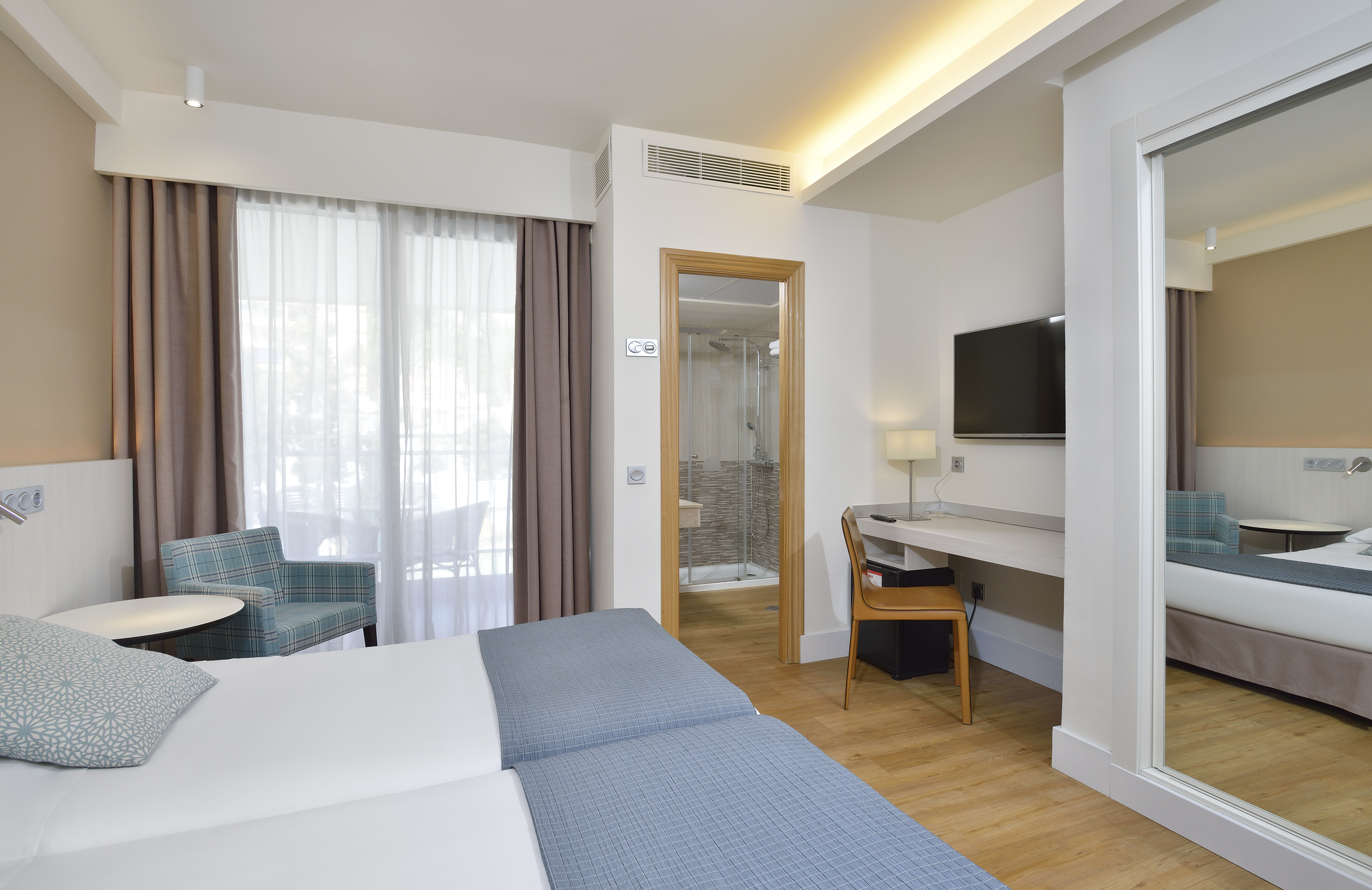 Modern hotel room with twin beds, desk, TV, and balcony access.