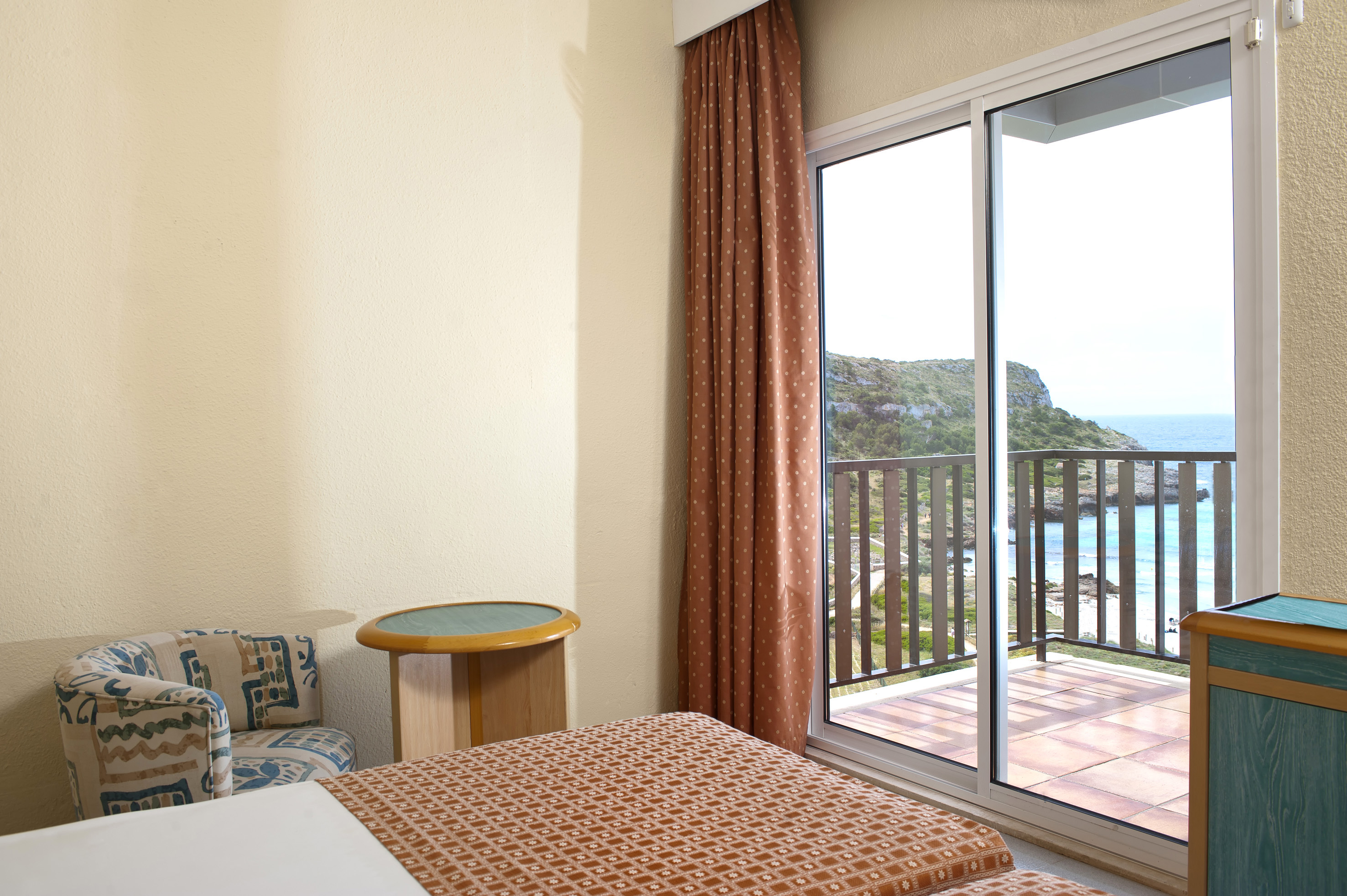 Hotel room with bed, armchair, and balcony with direct sea view over the coast.