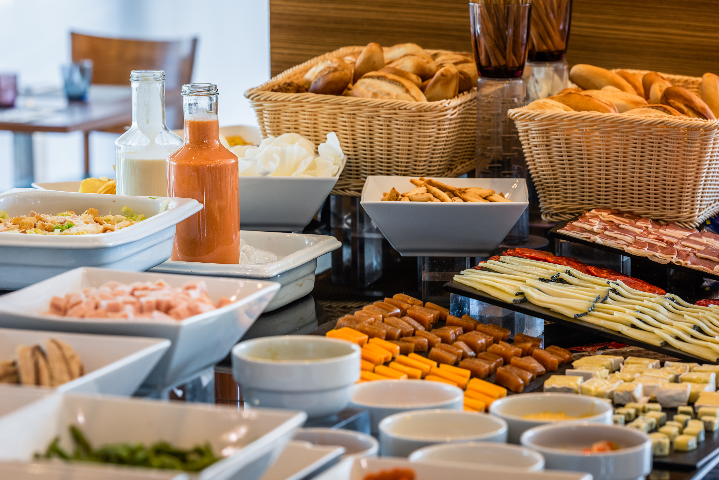 Hotel breakfast buffet with bread, cheese, sliced meats, salads, and drinks.