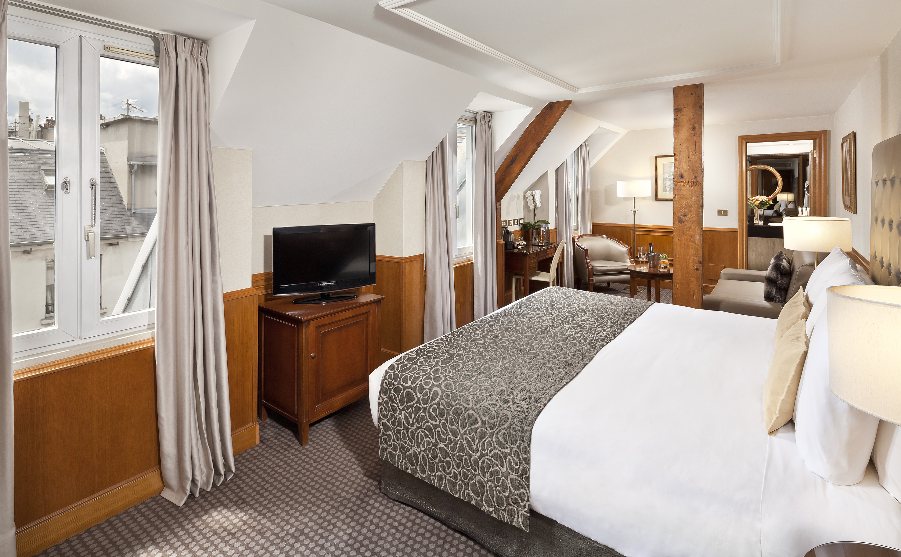 Luxurious attic hotel room with bed, TV, desk, and city view from window.