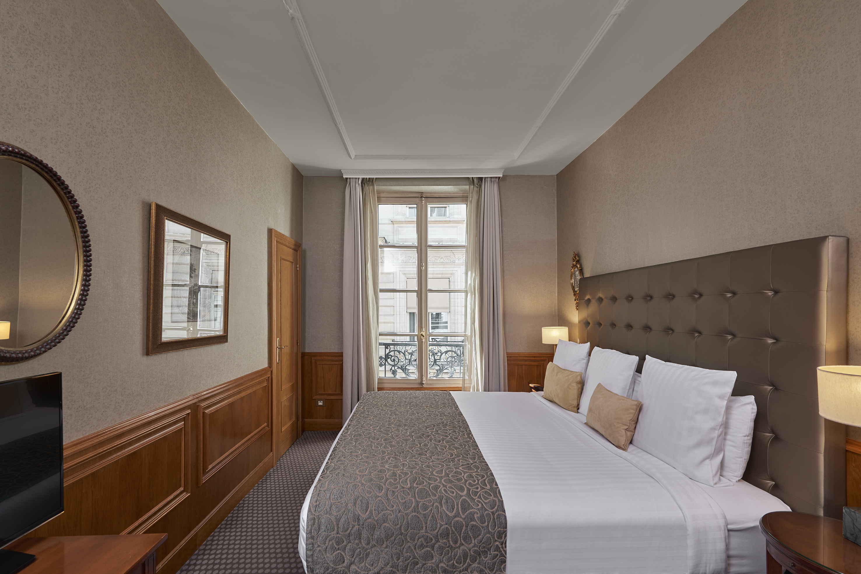 Elegant hotel bedroom with king bed, tufted headboard, and window view.