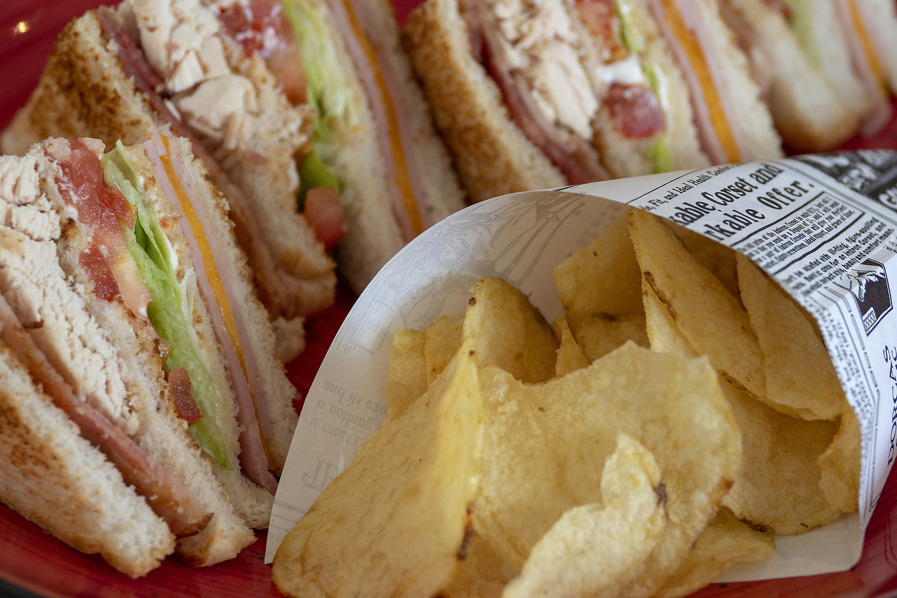 Toasted club sandwiches with lettuce, tomato, cheese, and chips on a red plate.