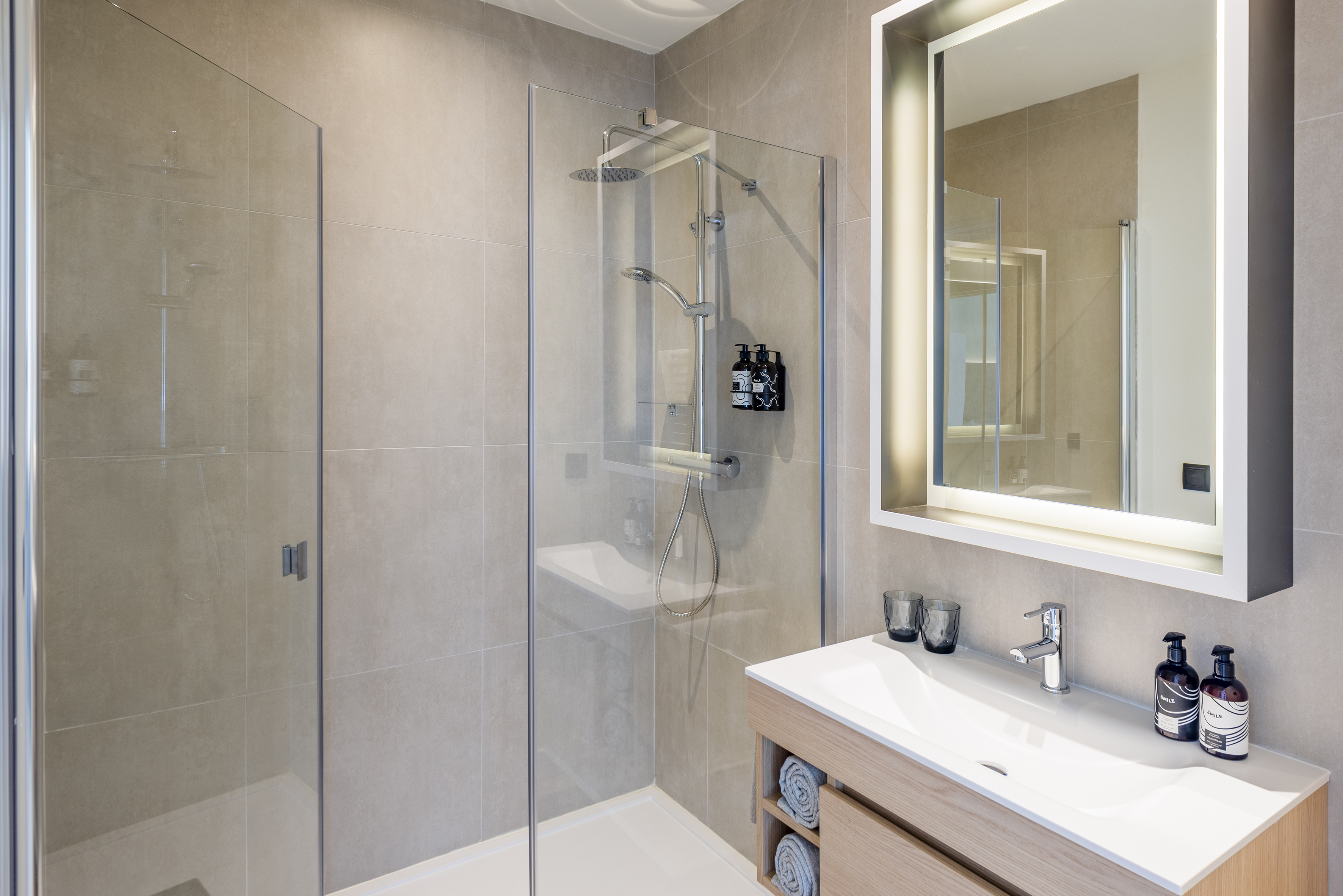 Contemporary bathroom with glass shower, wood vanity, and lighted mirror.