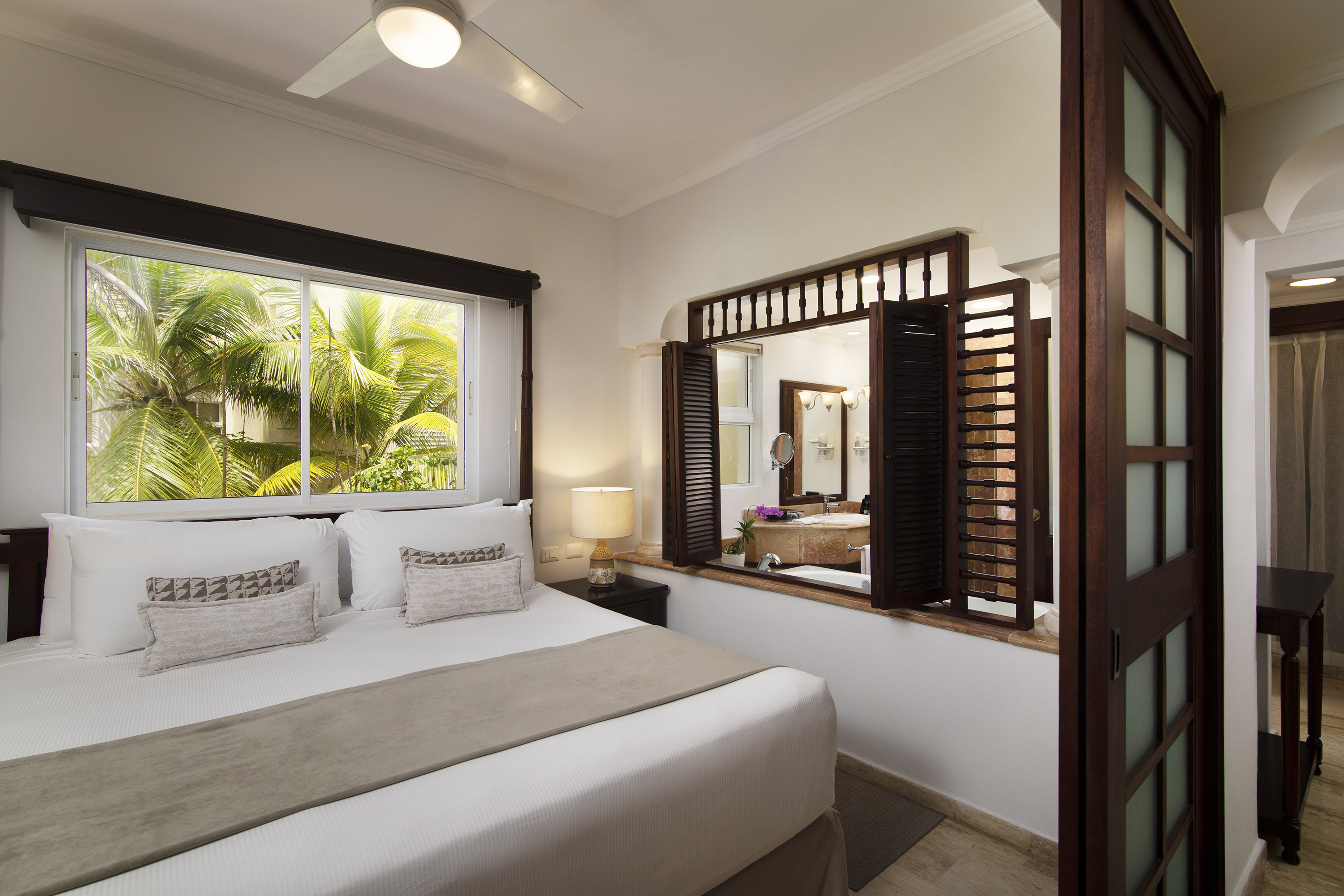 Tropical bedroom with bed, palm view, and open shutters to en-suite.