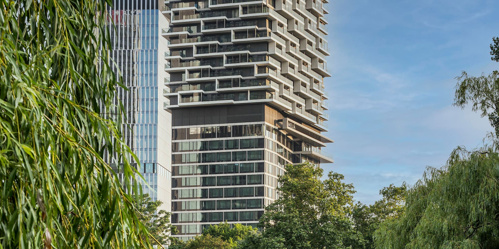Melia hotel skyscraper with staggered balconies overlooking a lake and willow.