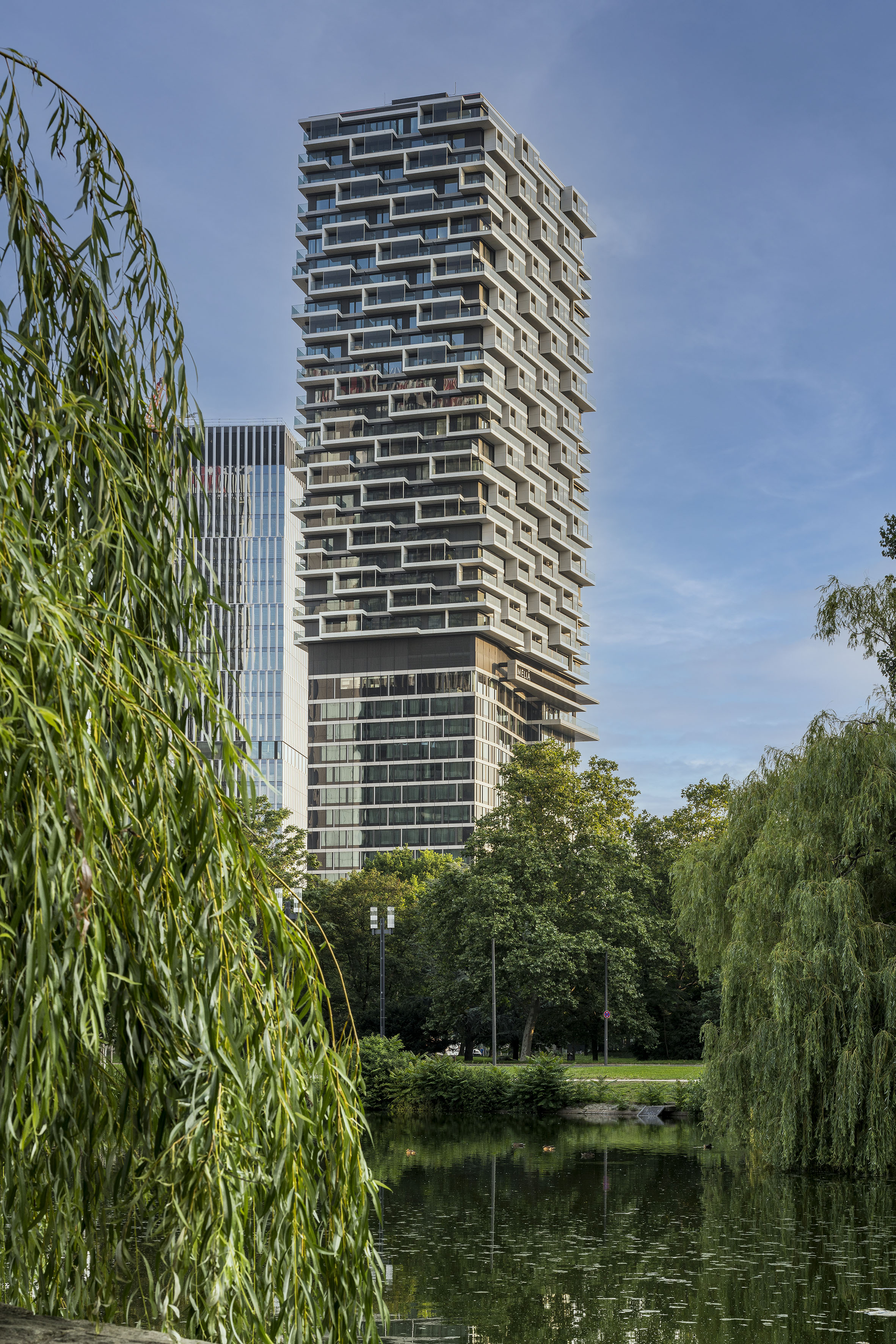 Melia hotel skyscraper with staggered balconies overlooking a lake and willow.