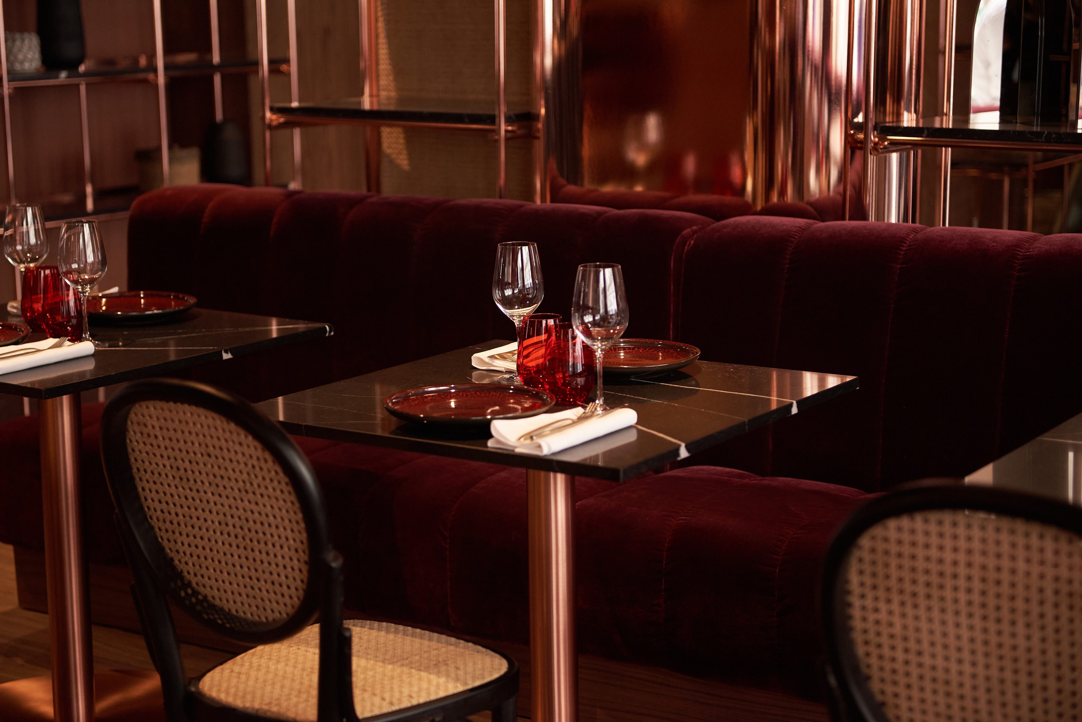 Elegant restaurant: red velvet booths, black marble tables, and copper accents.