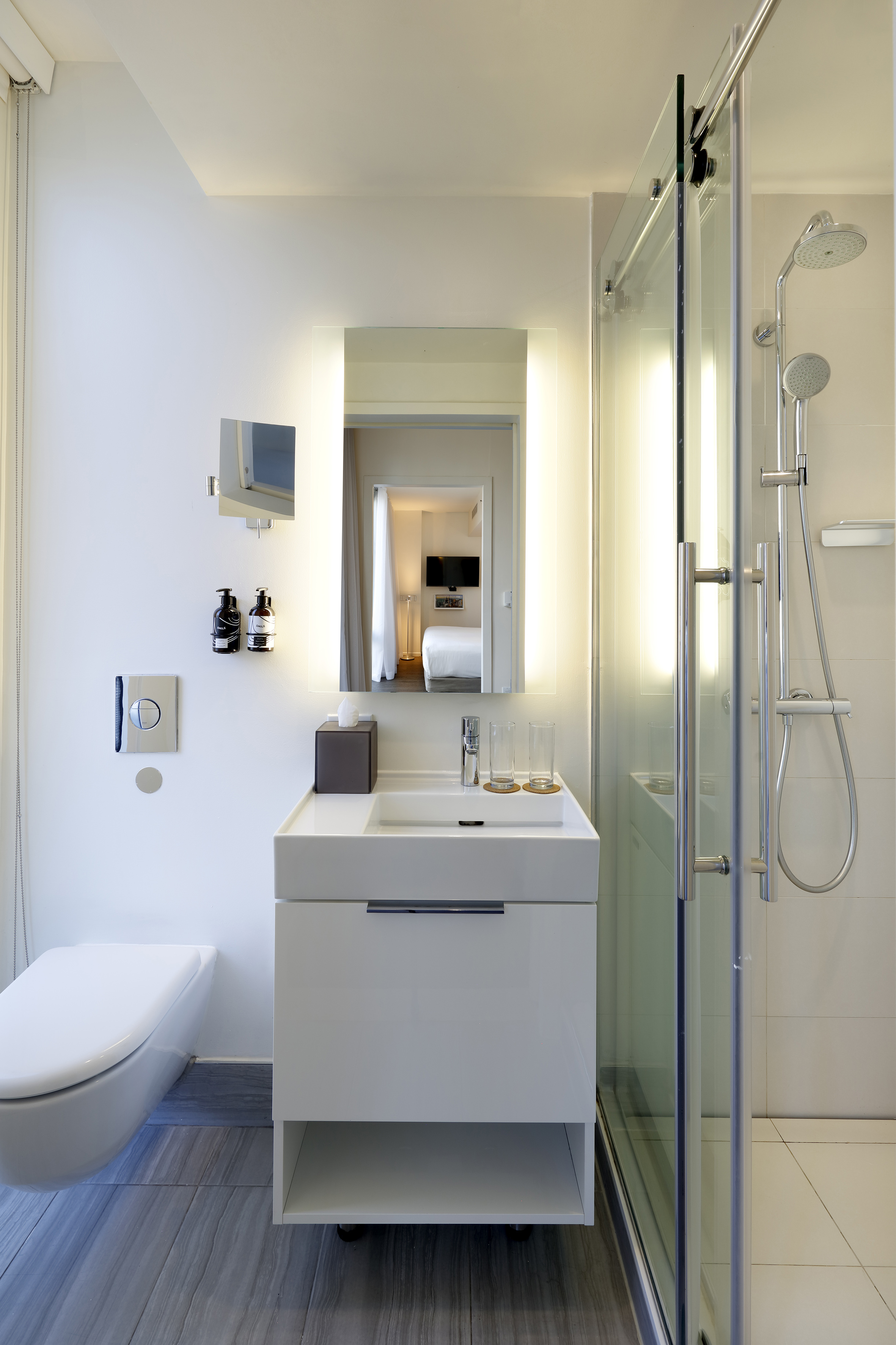 Modern bathroom with white vanity, backlit mirror, glass shower, and toilet.