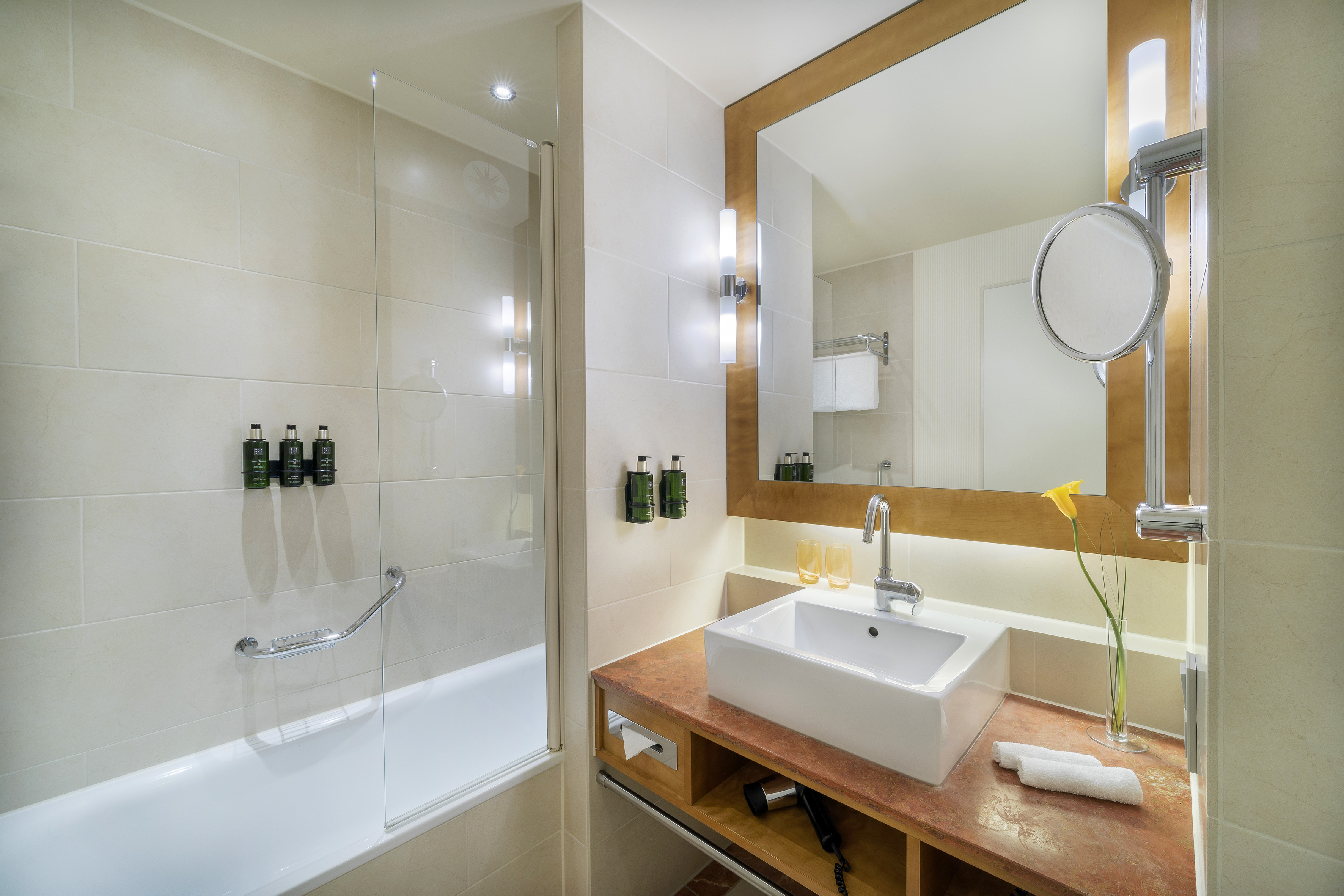 Modern hotel bathroom with bathtub, vanity sink, large mirror, and shower.