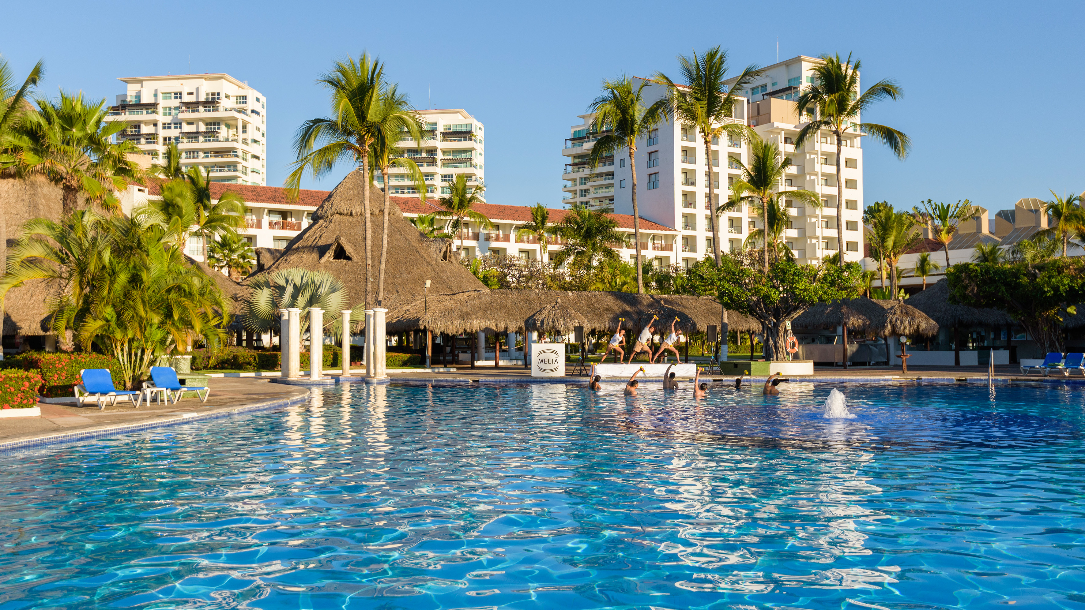 Melia hotel pool with water aerobics, palm trees, and resort buildings.