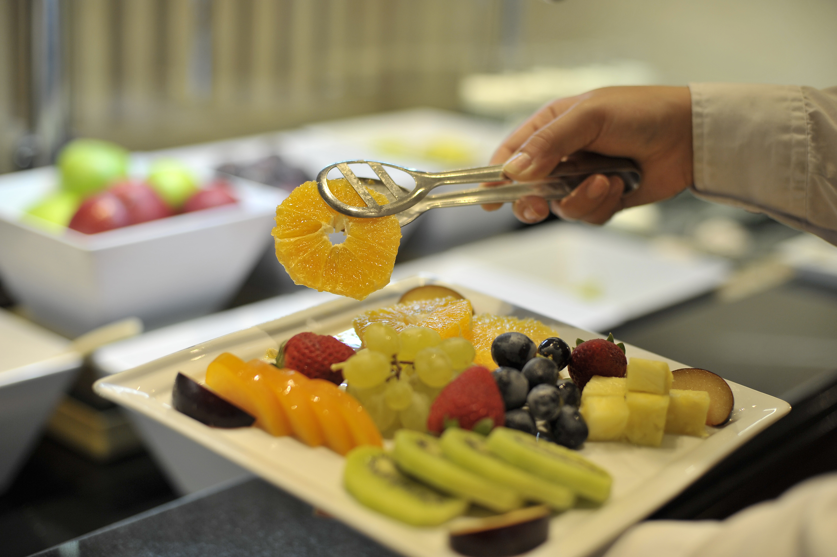 Hand picking orange slice from a vibrant fruit platter at a healthy buffet.