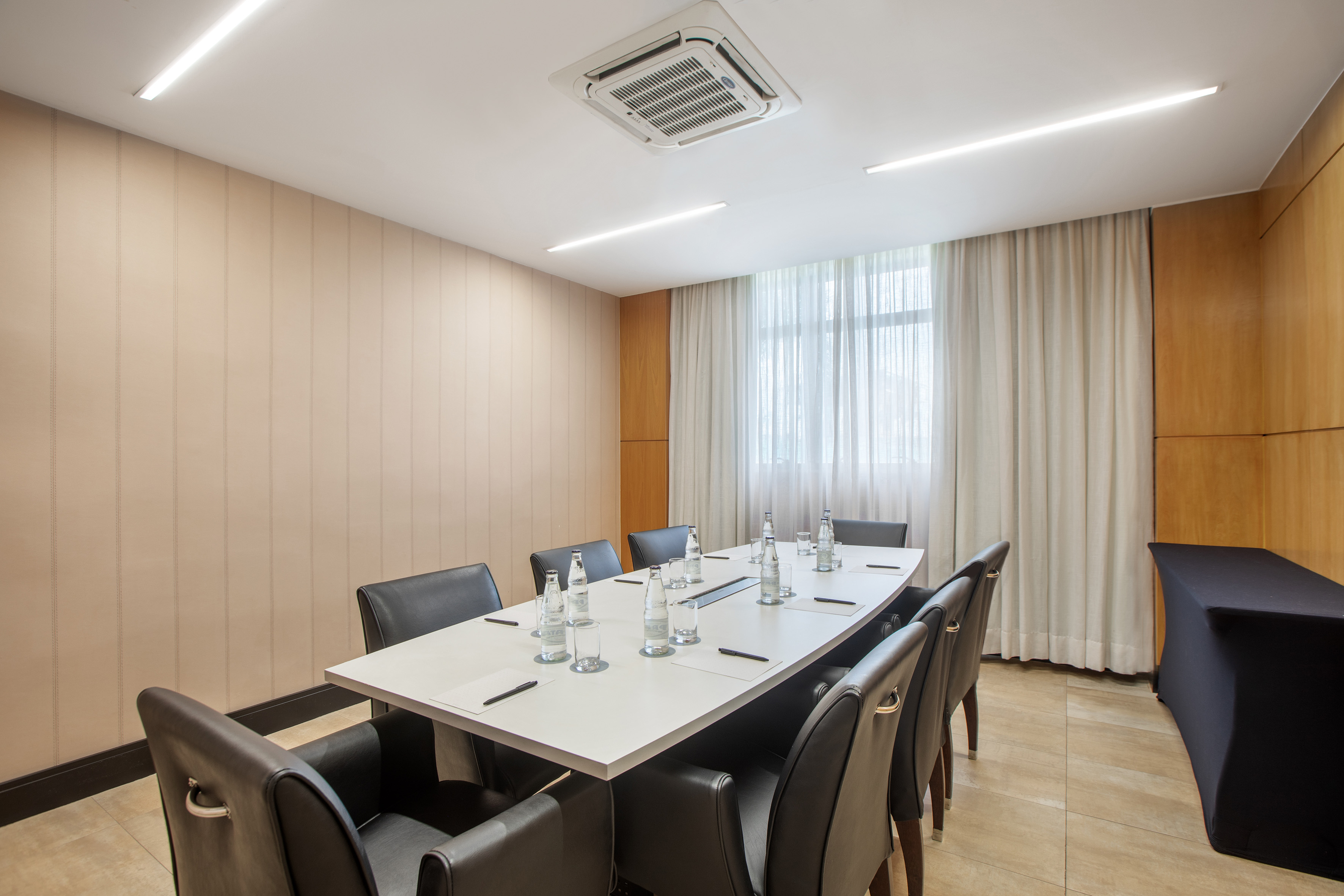 Modern meeting room with long white table, dark chairs, and bright window.