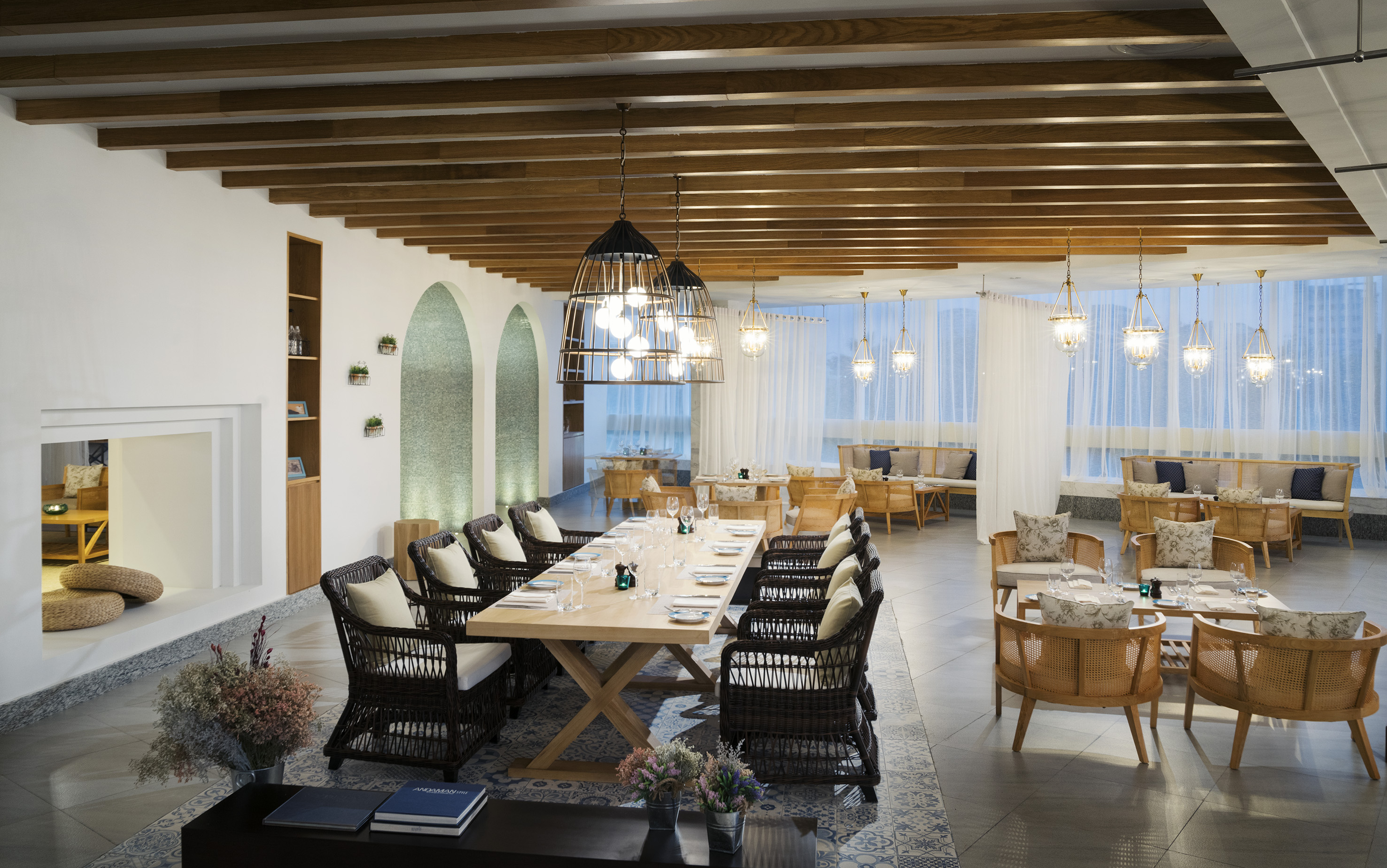 Resort dining room with long wooden table, rattan chairs, and chandeliers.