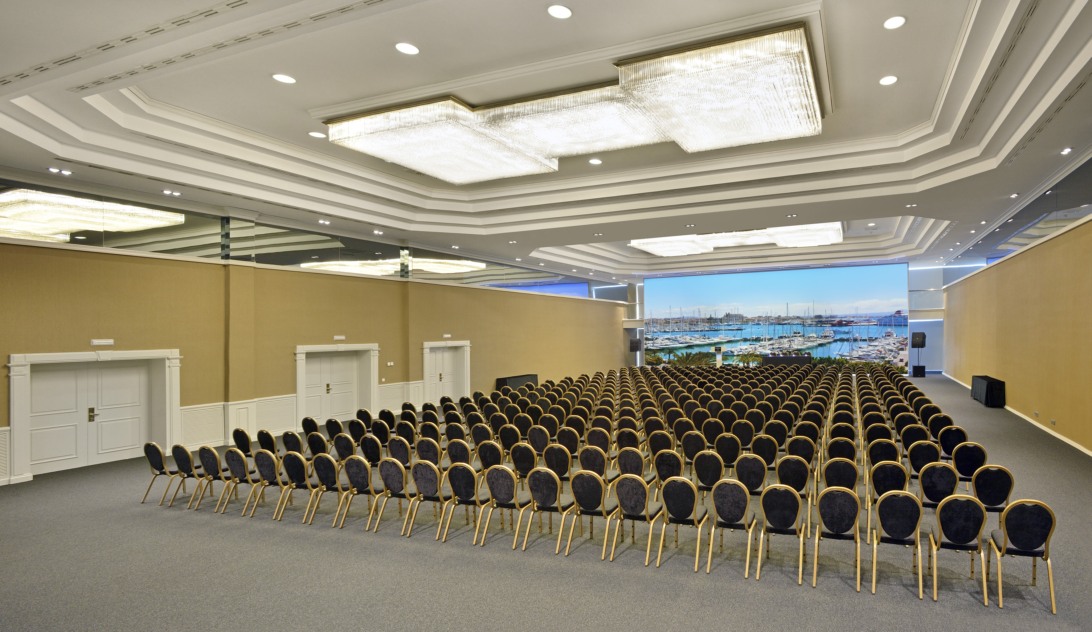 Spacious conference hall, rows of chairs, large screen with marina view.