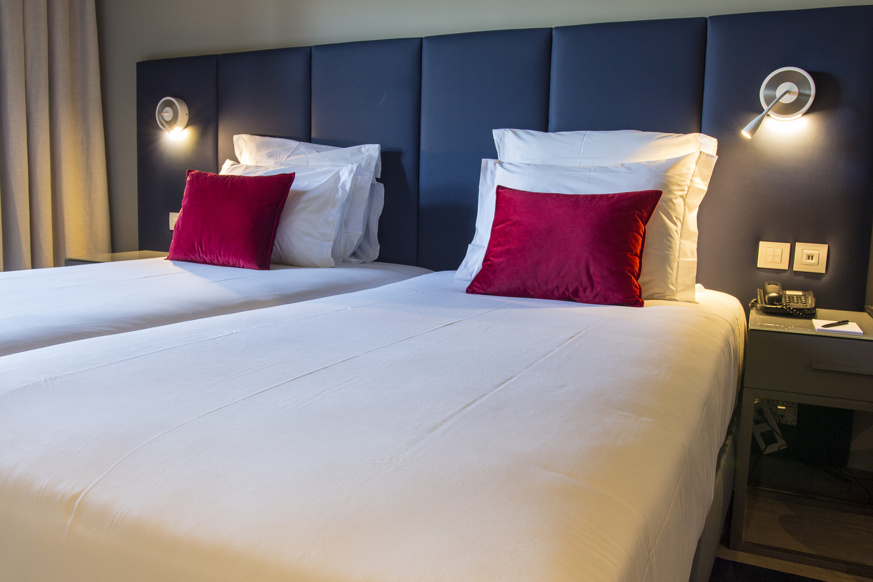 Hotel room with twin beds, white bedding, red pillows, and blue headboards.