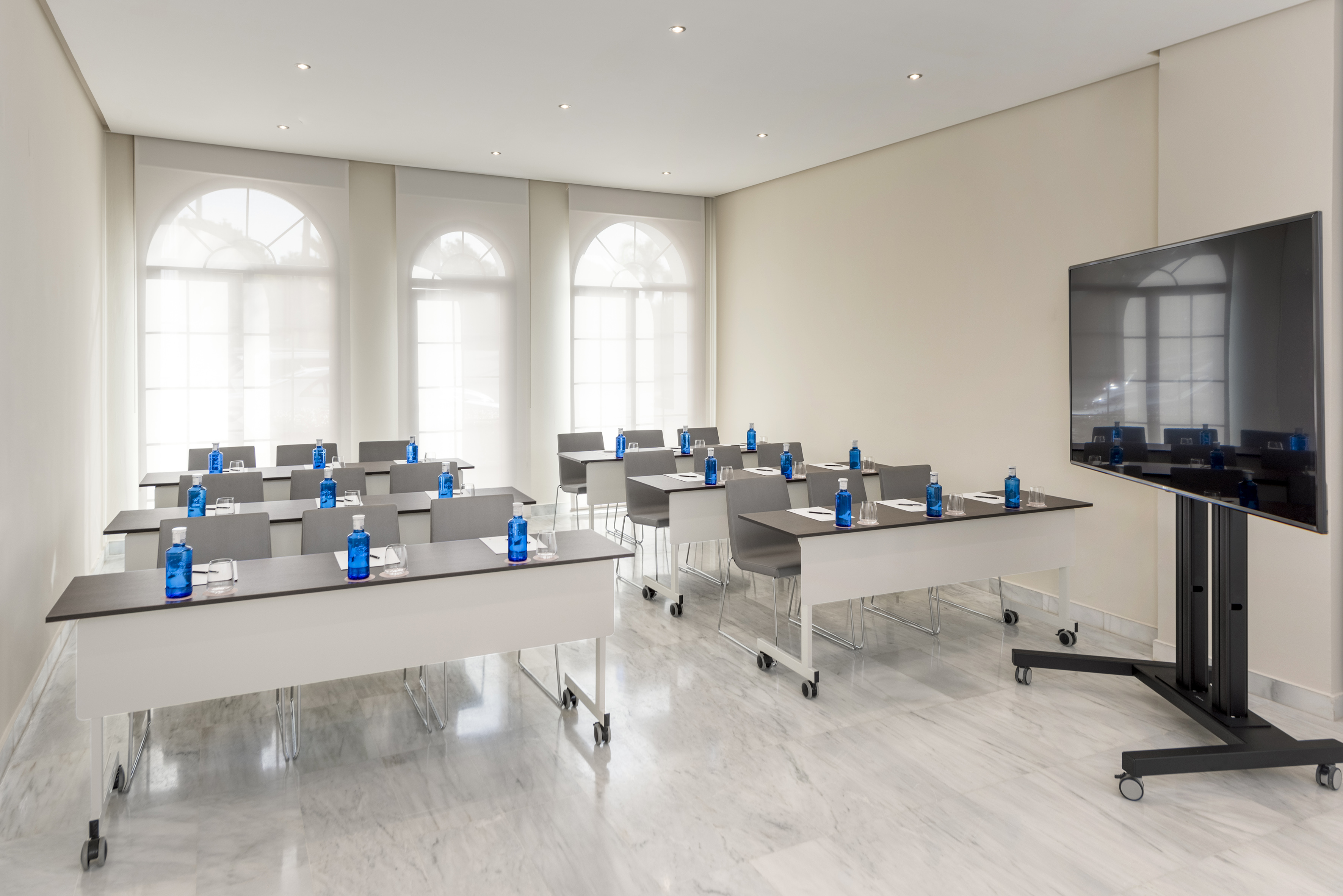 Contemporary training room with tables, water, large screen, and arched windows.