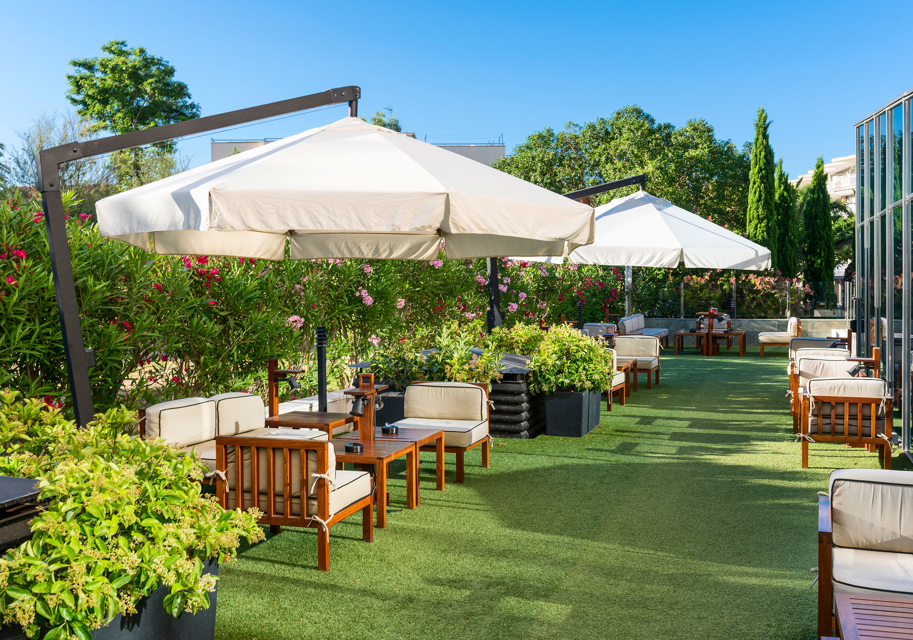 Sunny outdoor patio with wooden lounge chairs, shade umbrellas, and green turf.