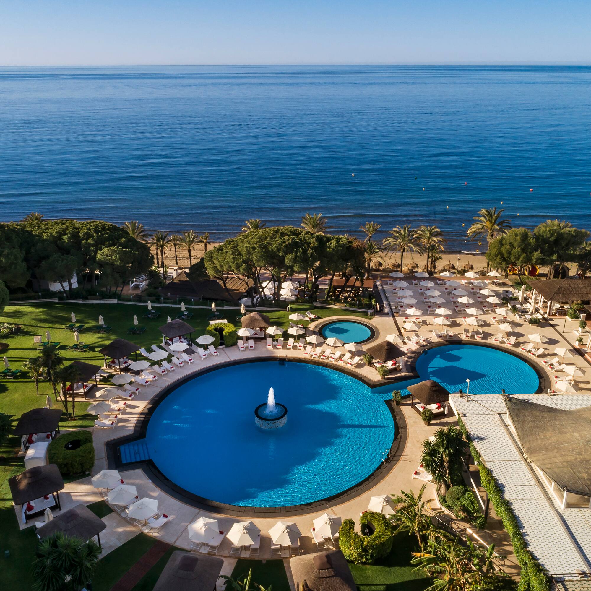 a swimming pool with a fountain surrounded by trees and a body of water