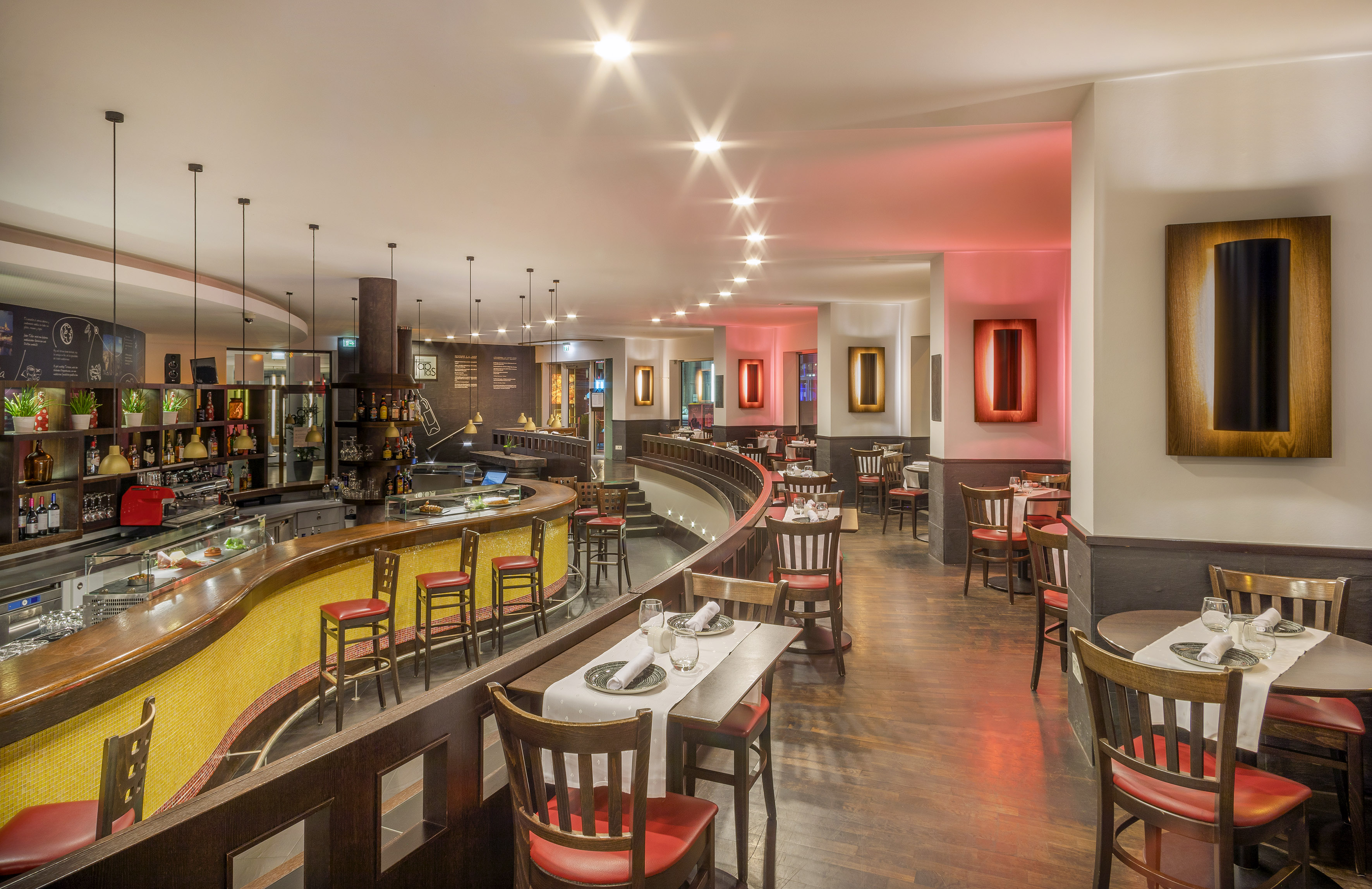 Modern restaurant bar, dining area with red chairs, and warm lighting. - Meliá Tapas Bar, Tapas - Meliá Berlin, Berlijn