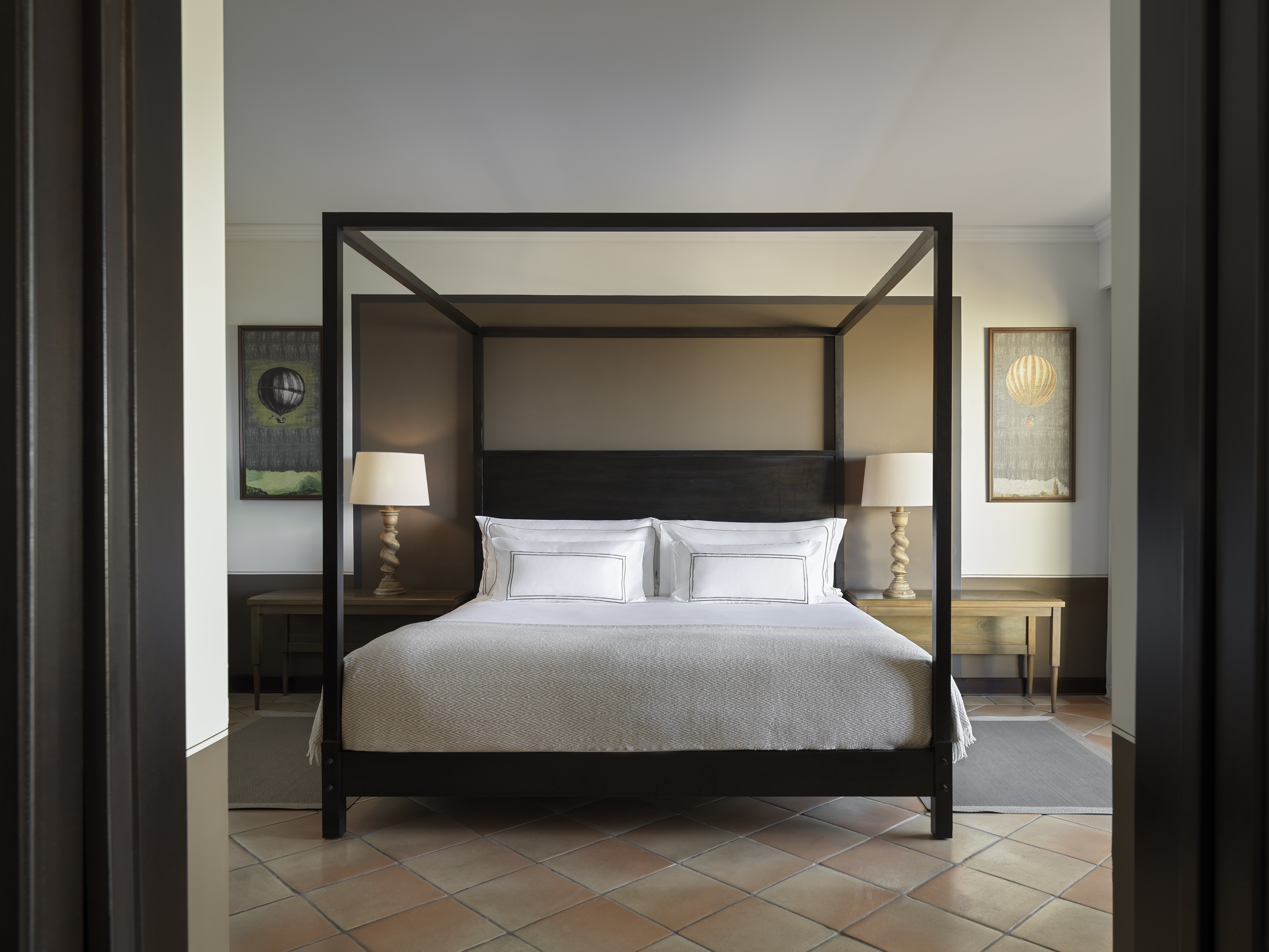 Luxury hotel bedroom with dark four-poster bed and terracotta tiles.