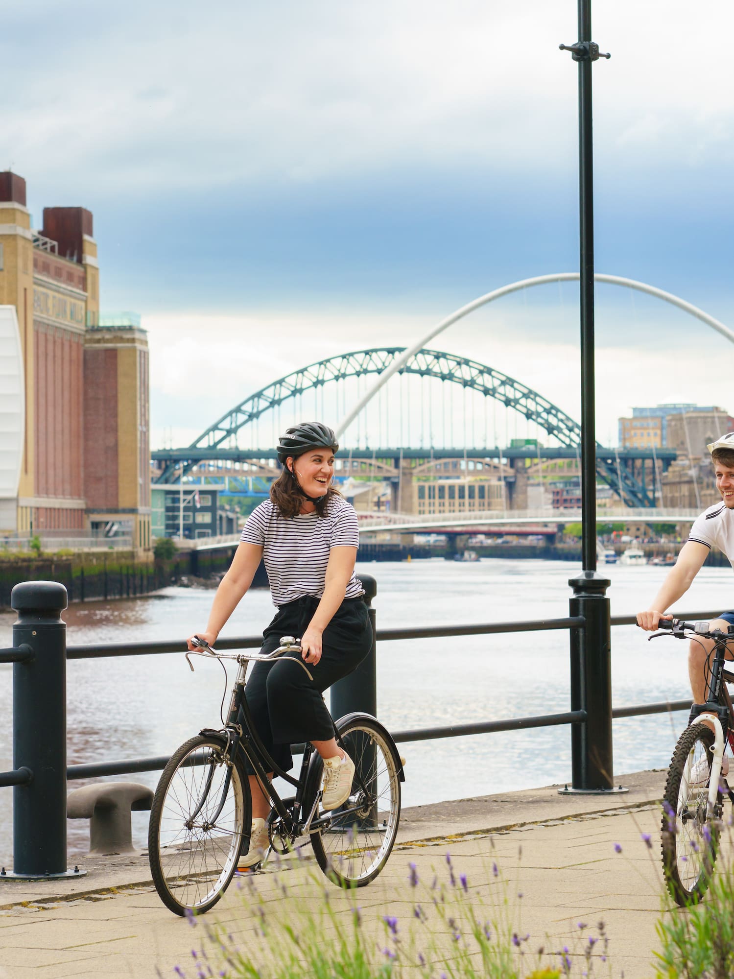 a man and woman riding bikes on a sidewalk by a river