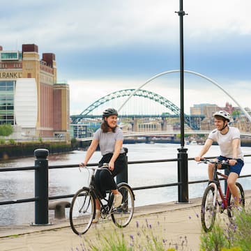 a man and woman riding bikes on a sidewalk by a river