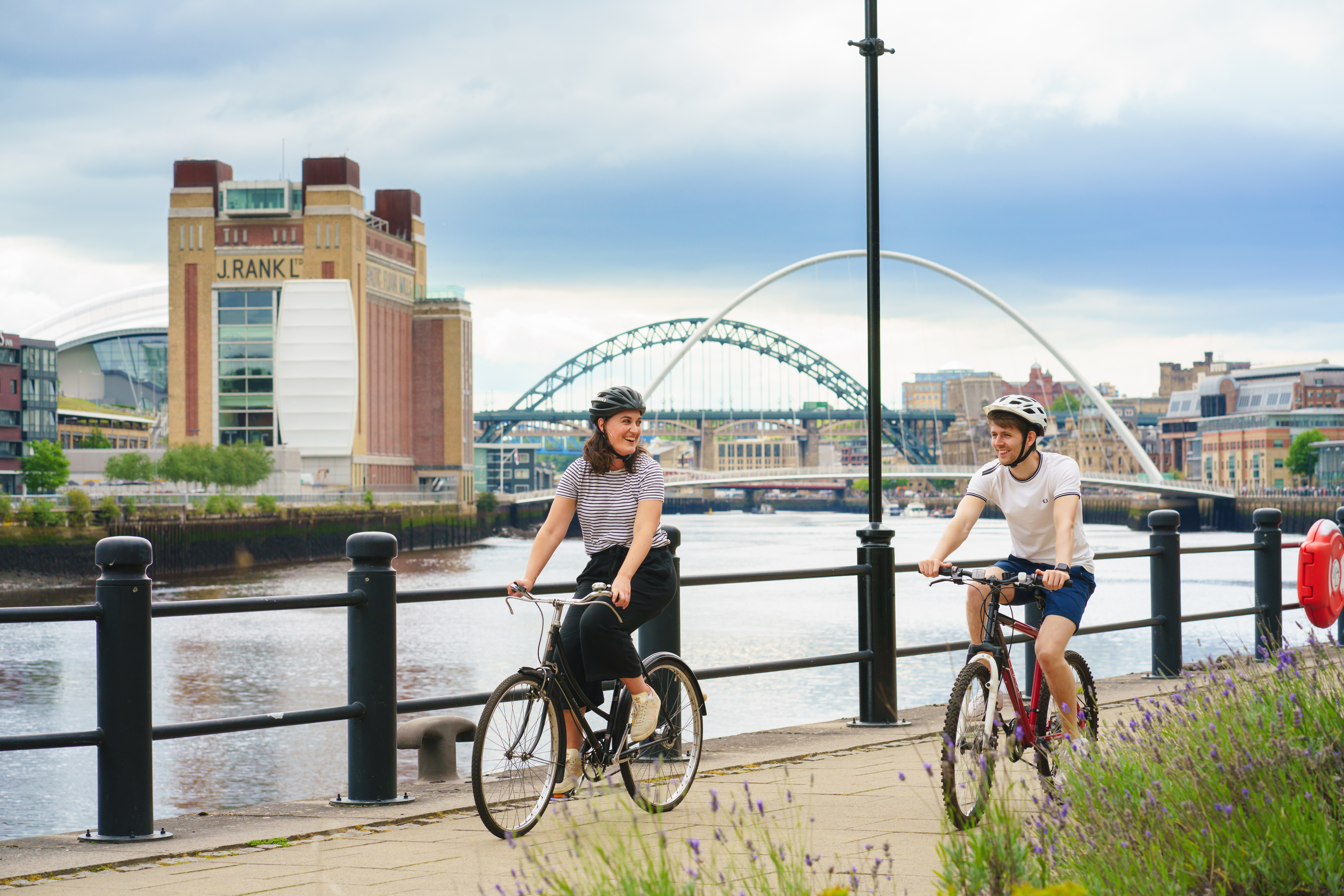 a man and woman riding bikes on a sidewalk by a river