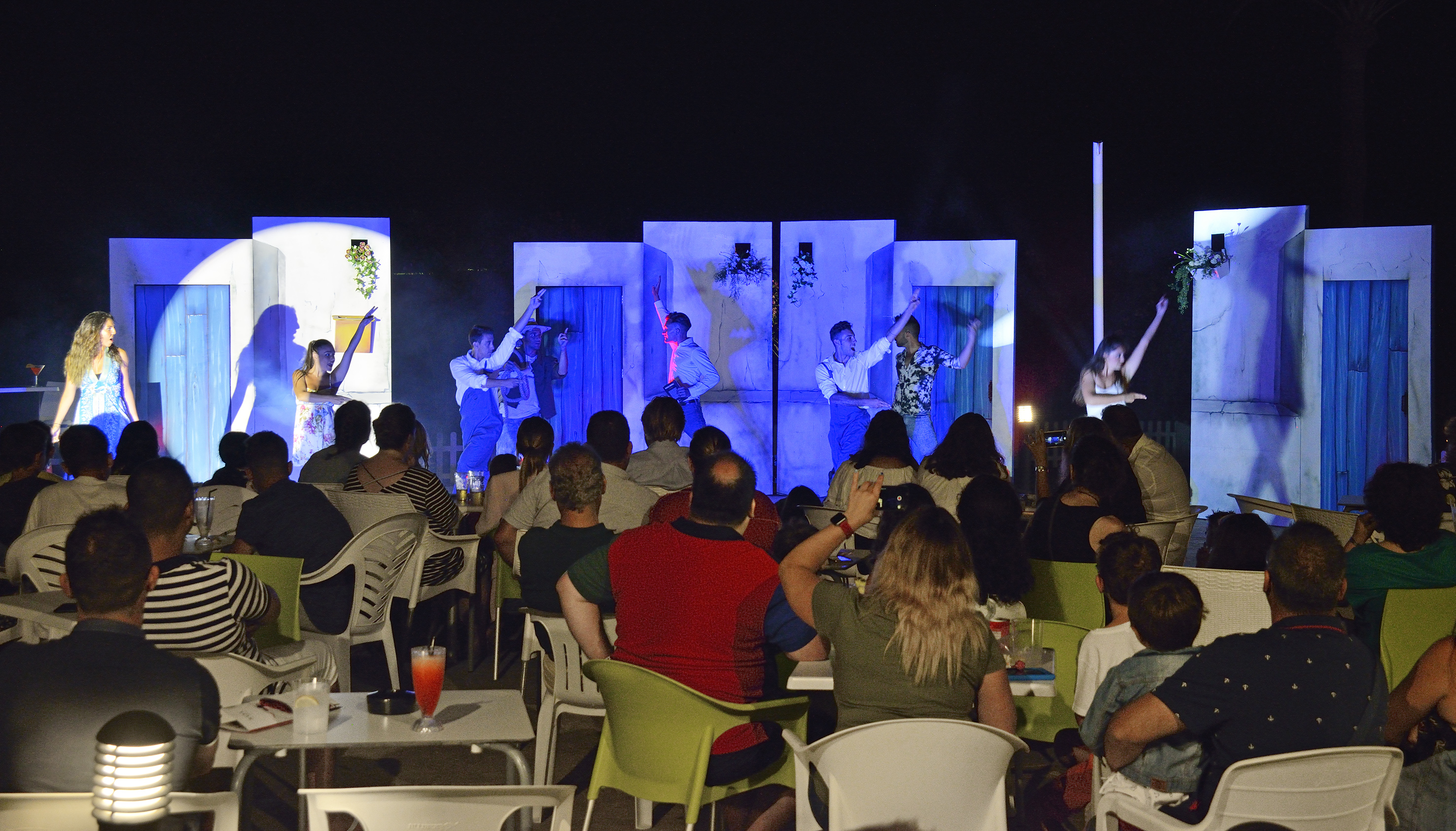 Audience enjoying a Greek-themed outdoor live stage performance at night.