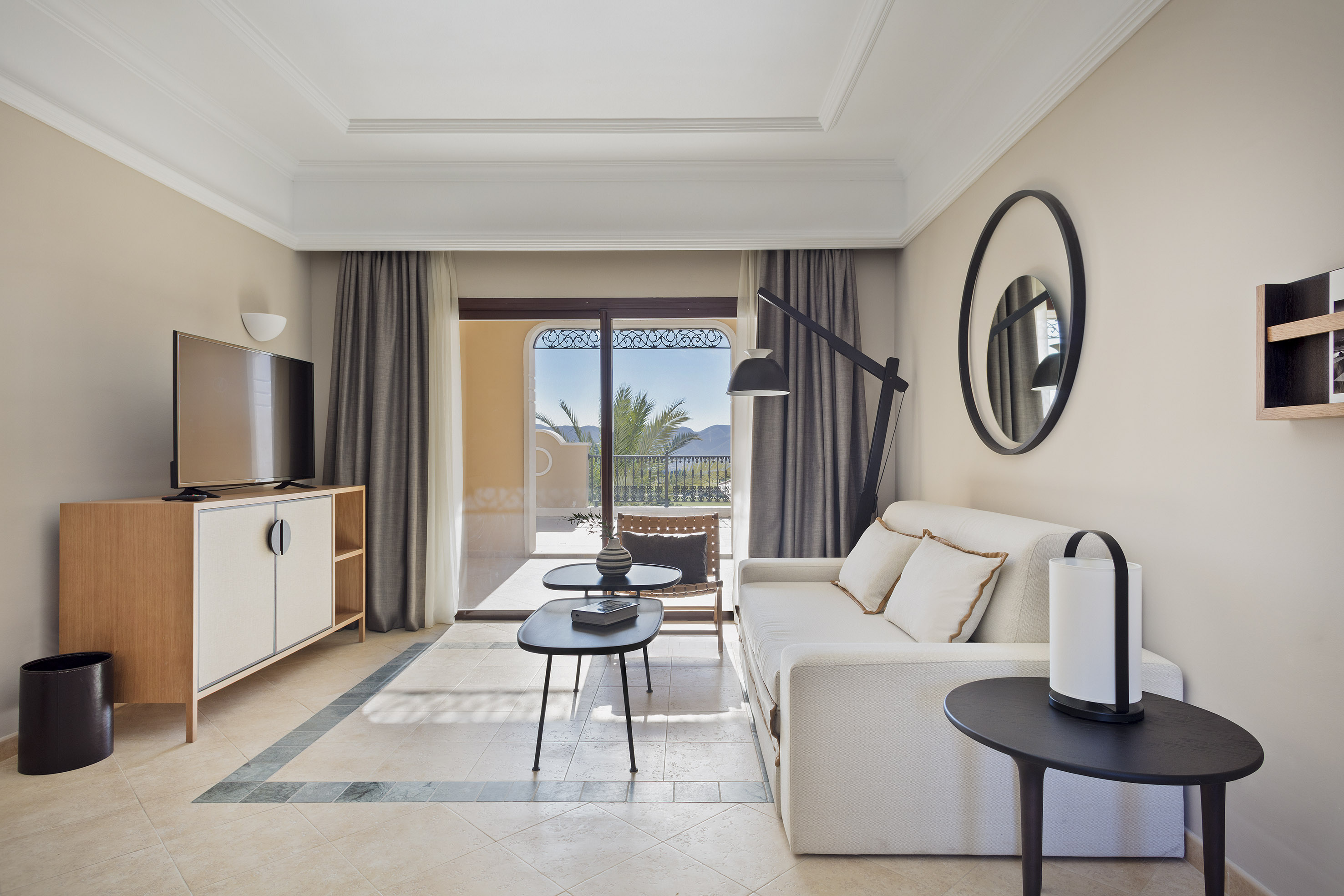 Modern hotel suite living room with balcony, sofa, TV, and mountain view.