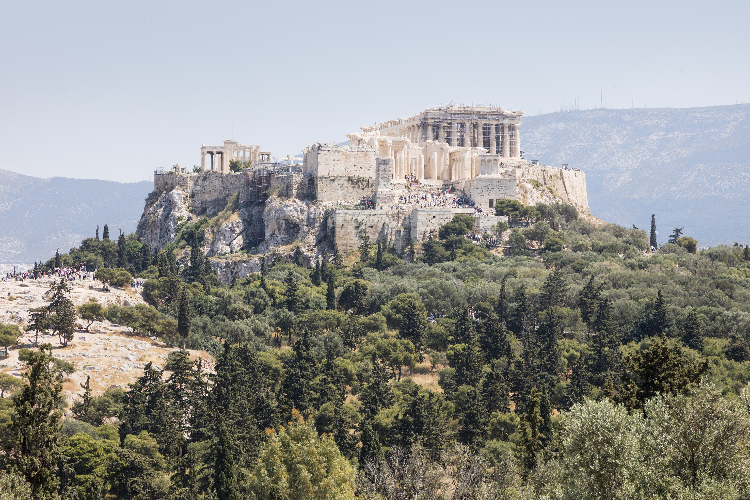 Parthenon temple on Acropolis of Athens hill, surrounded by green landscape.