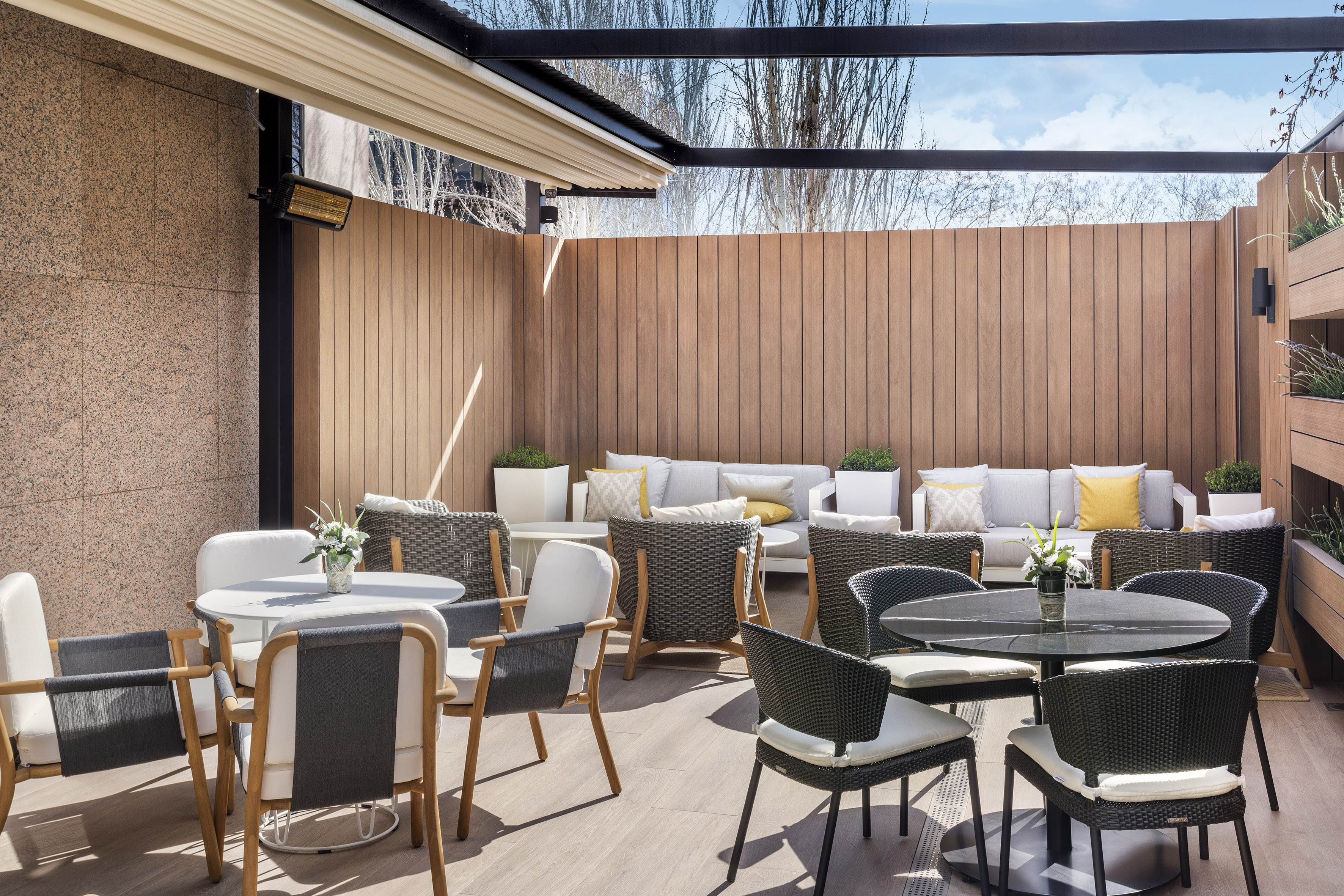 Modern outdoor patio with dining tables, lounge sofas, and wooden privacy walls.