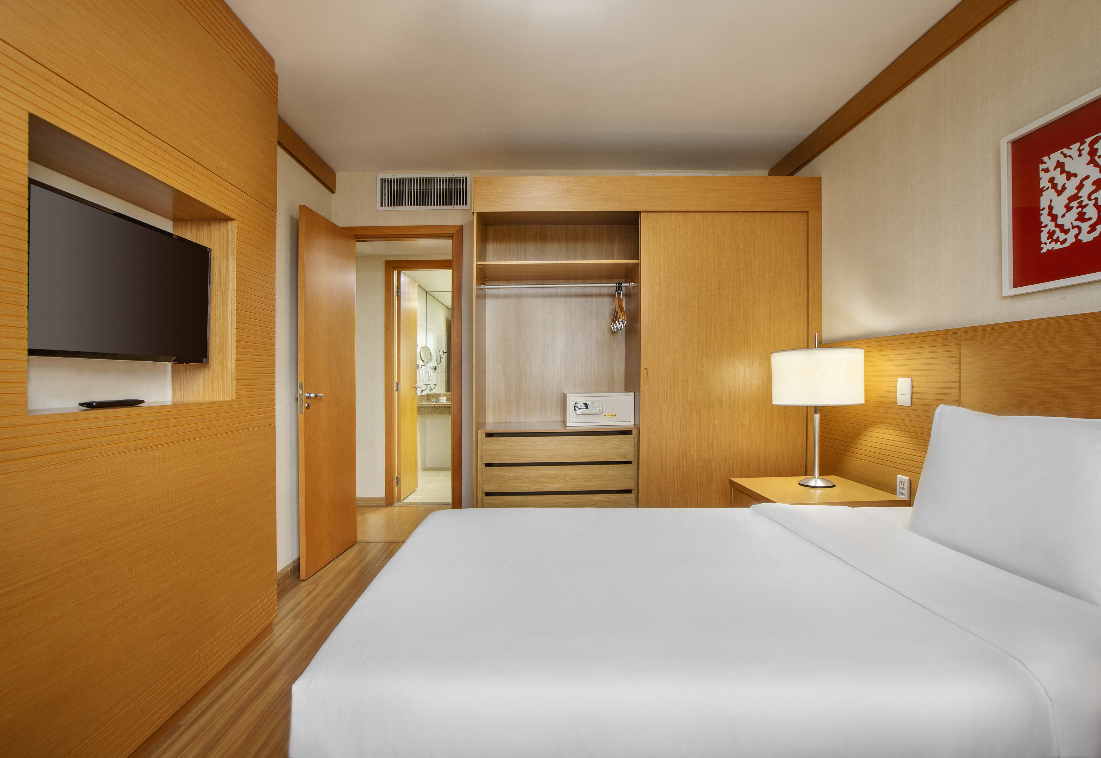 Contemporary hotel room with bed, TV, wooden closet, and bathroom.