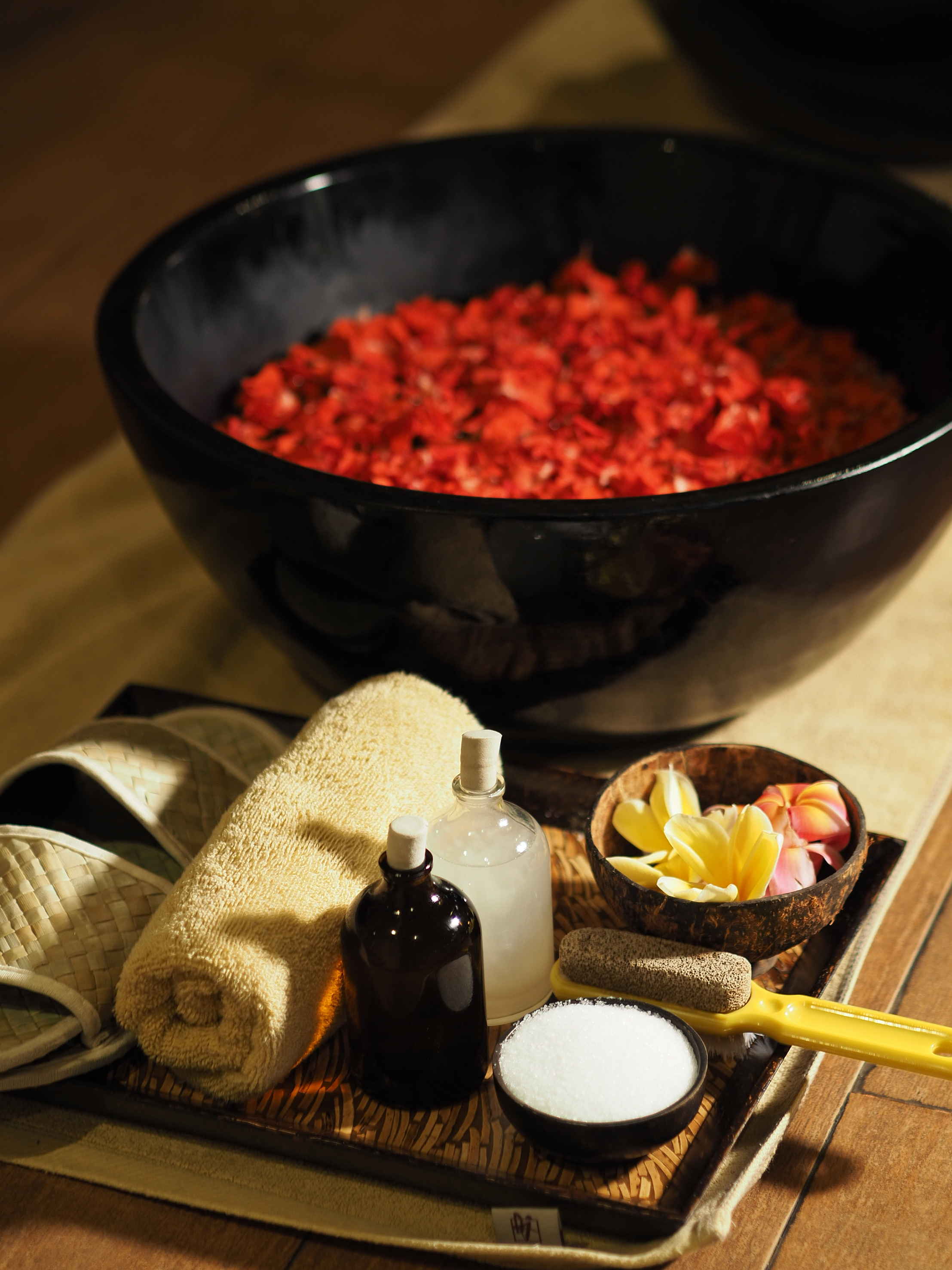 a bowl of red petals and a towel and a bottle of salt