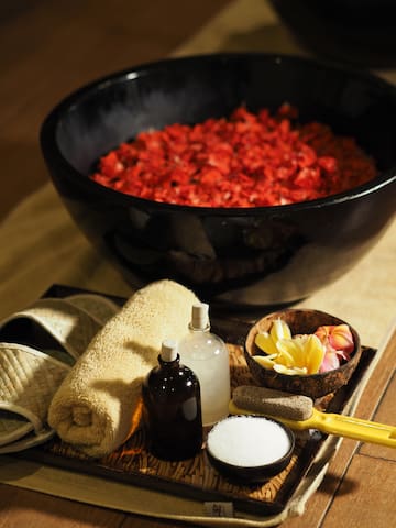 a bowl of red petals and a towel and a bottle of salt