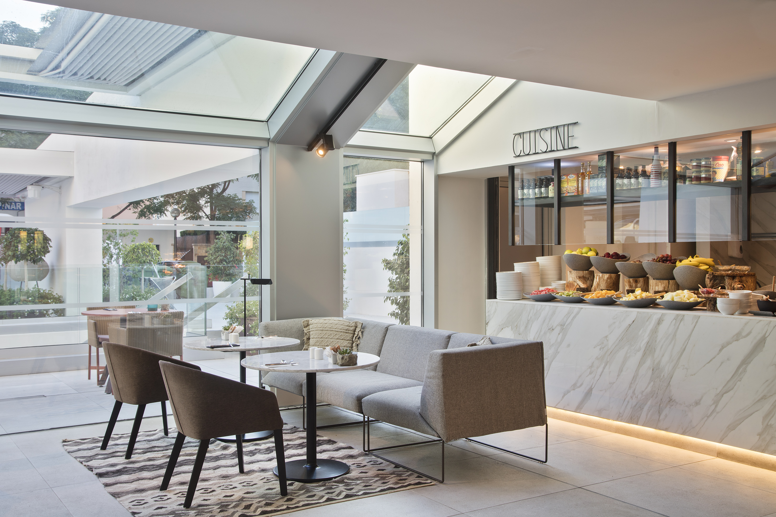 Modern hotel lounge with breakfast buffet, comfortable seating, and glass roof.