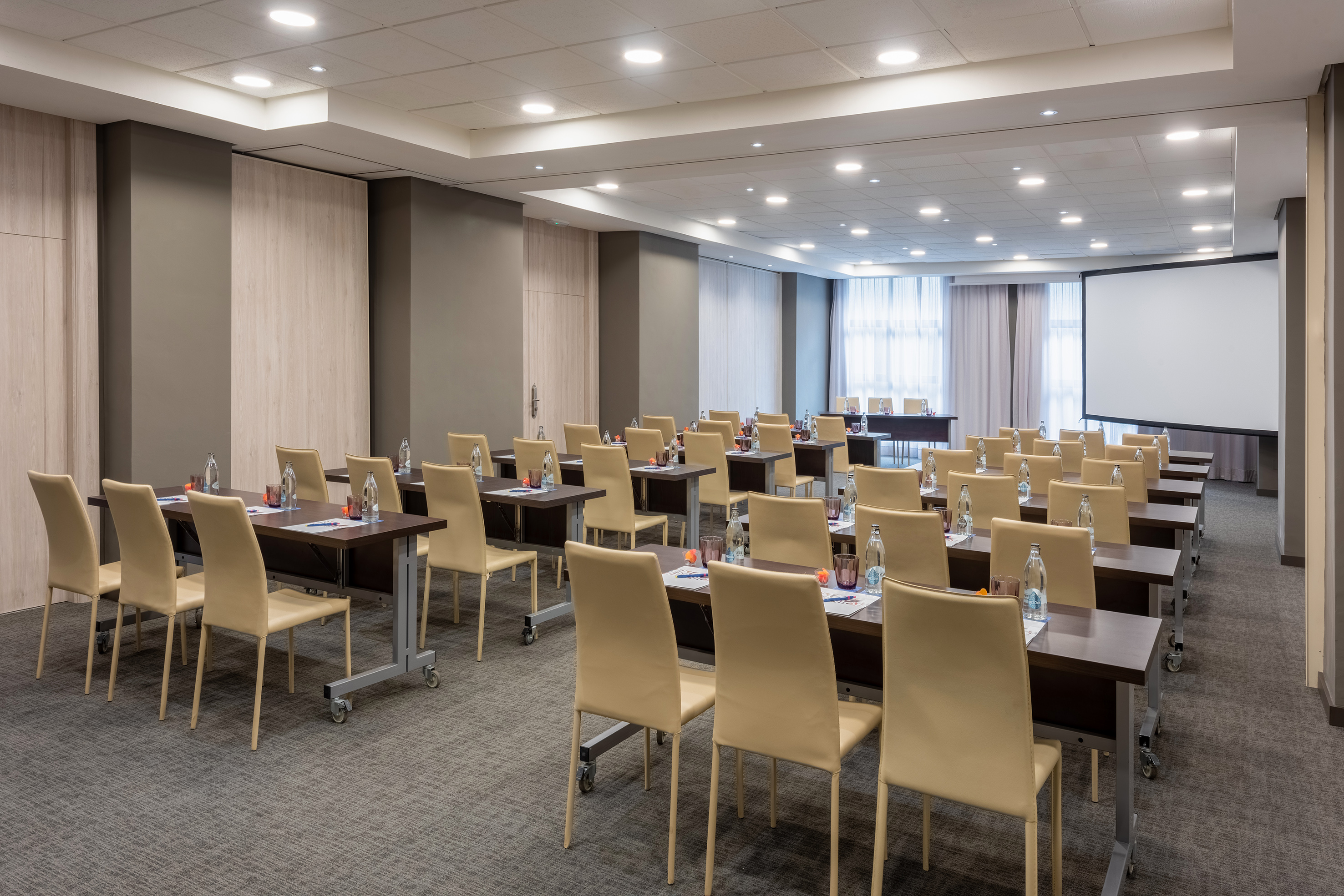 Modern training room with rows of tables, chairs, and large projection screen.