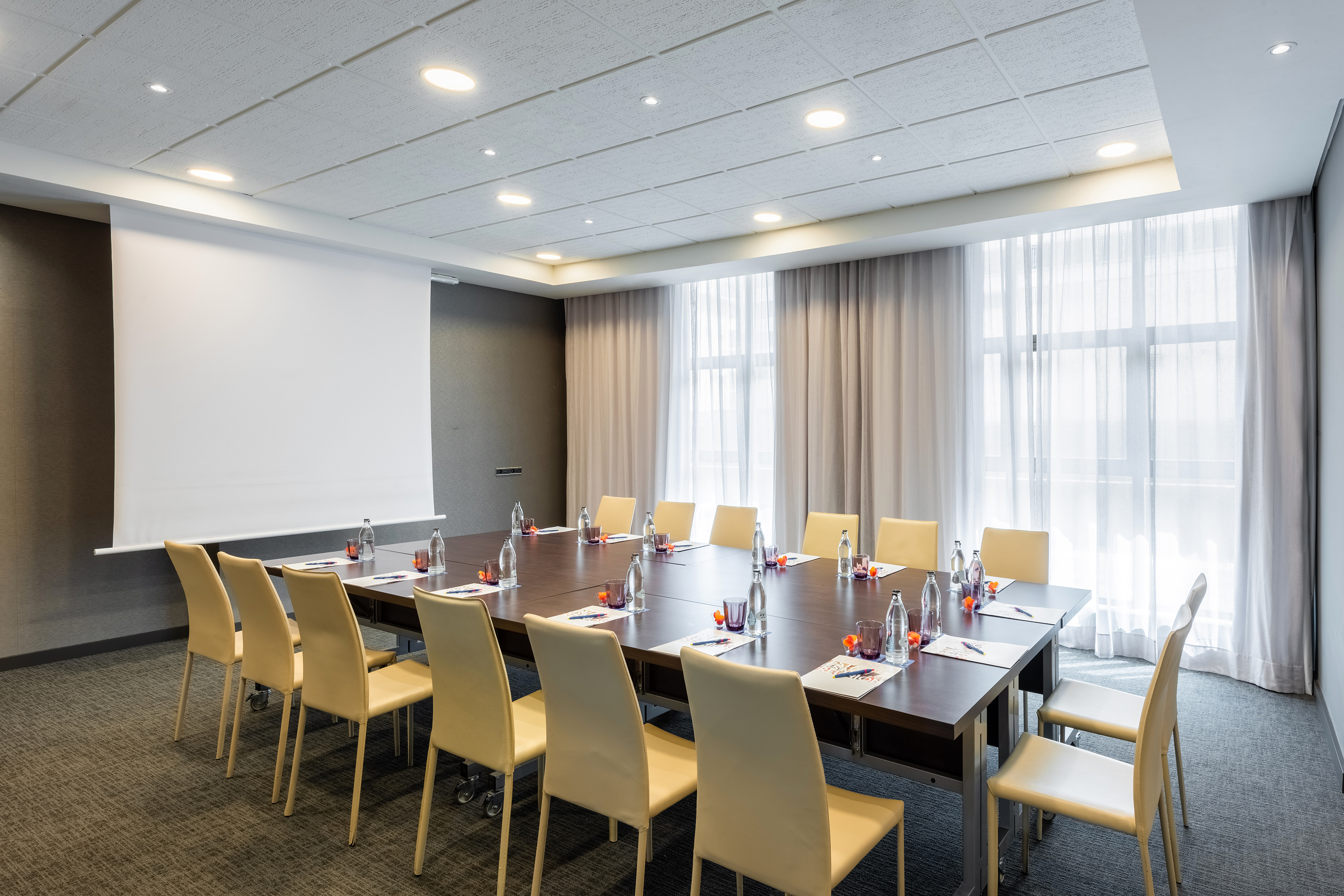Modern meeting room with large table, beige chairs, and projector screen.