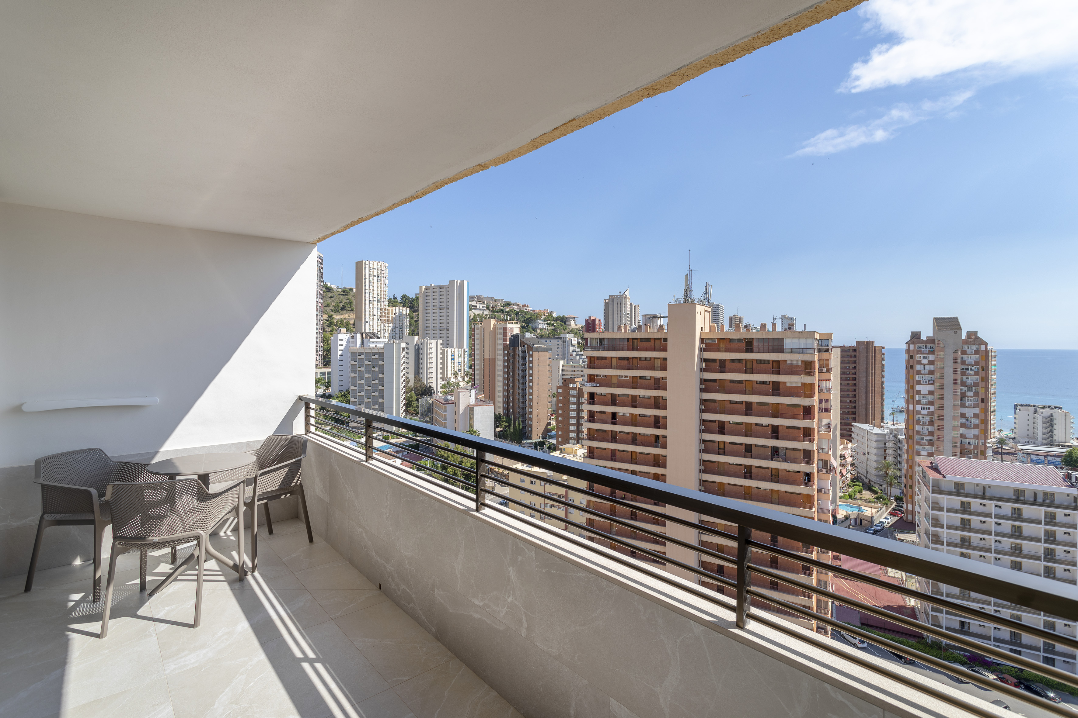 Sunny balcony with table, chairs, city skyline, and ocean view.