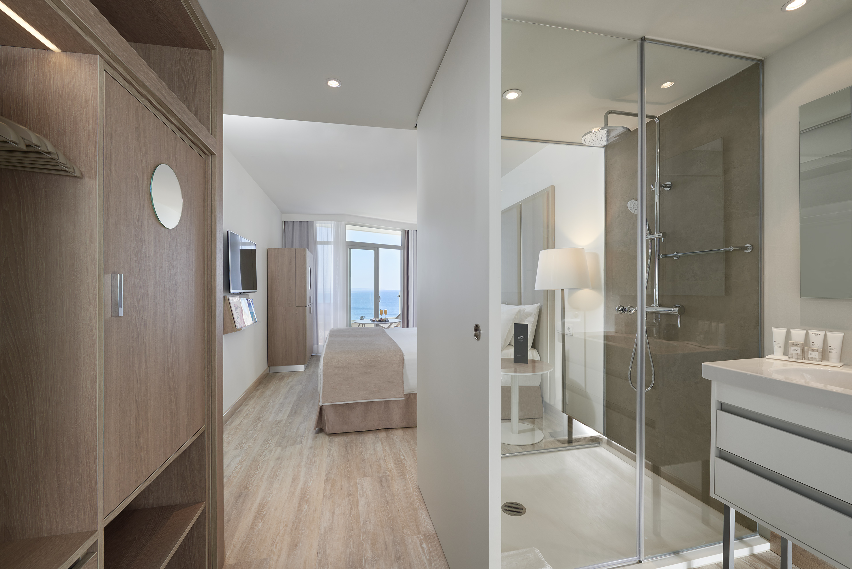 Contemporary hotel suite with ocean view, bed, and glass shower.