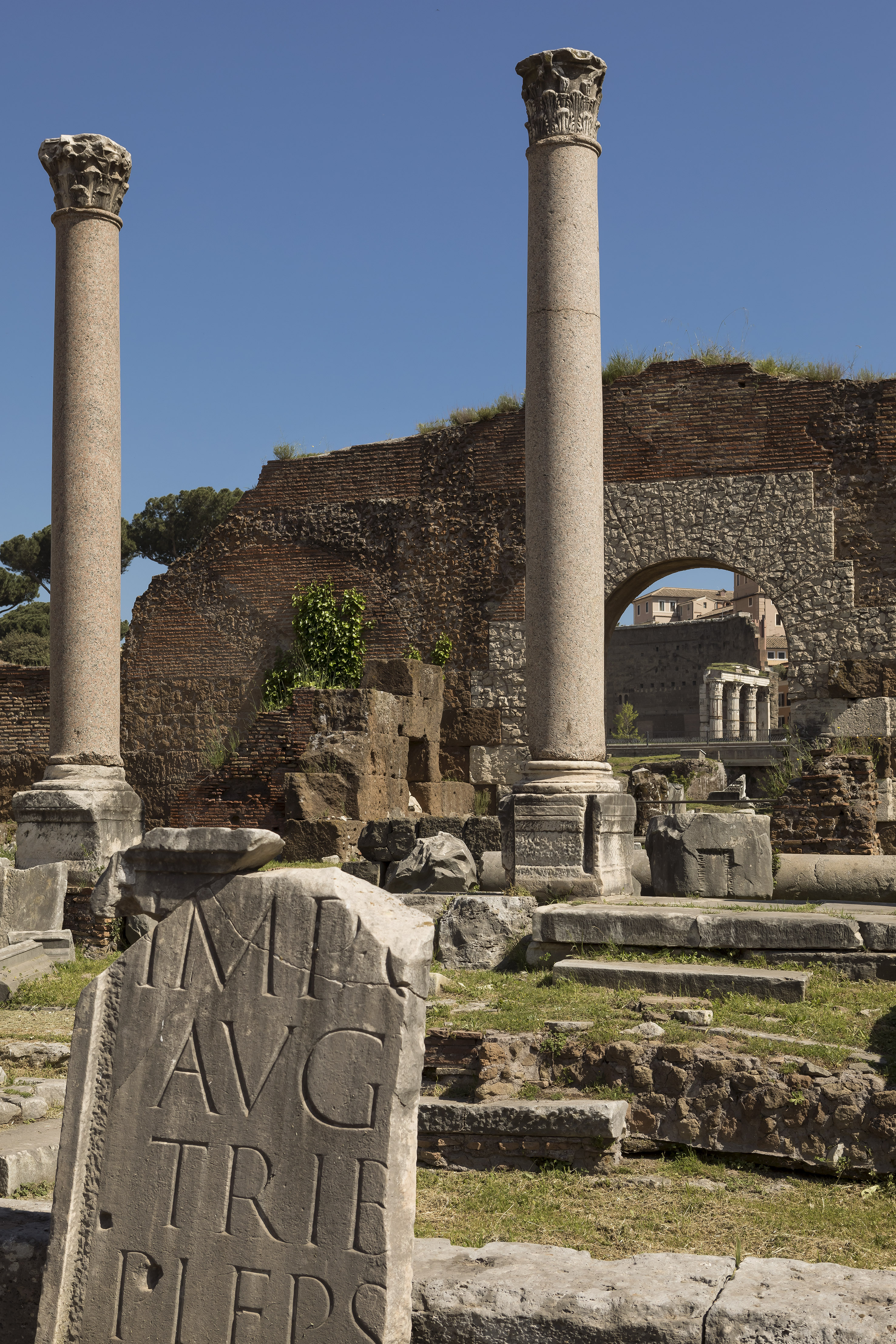 Historic Roman Forum ruins: two ancient columns, stone inscription, brick walls.